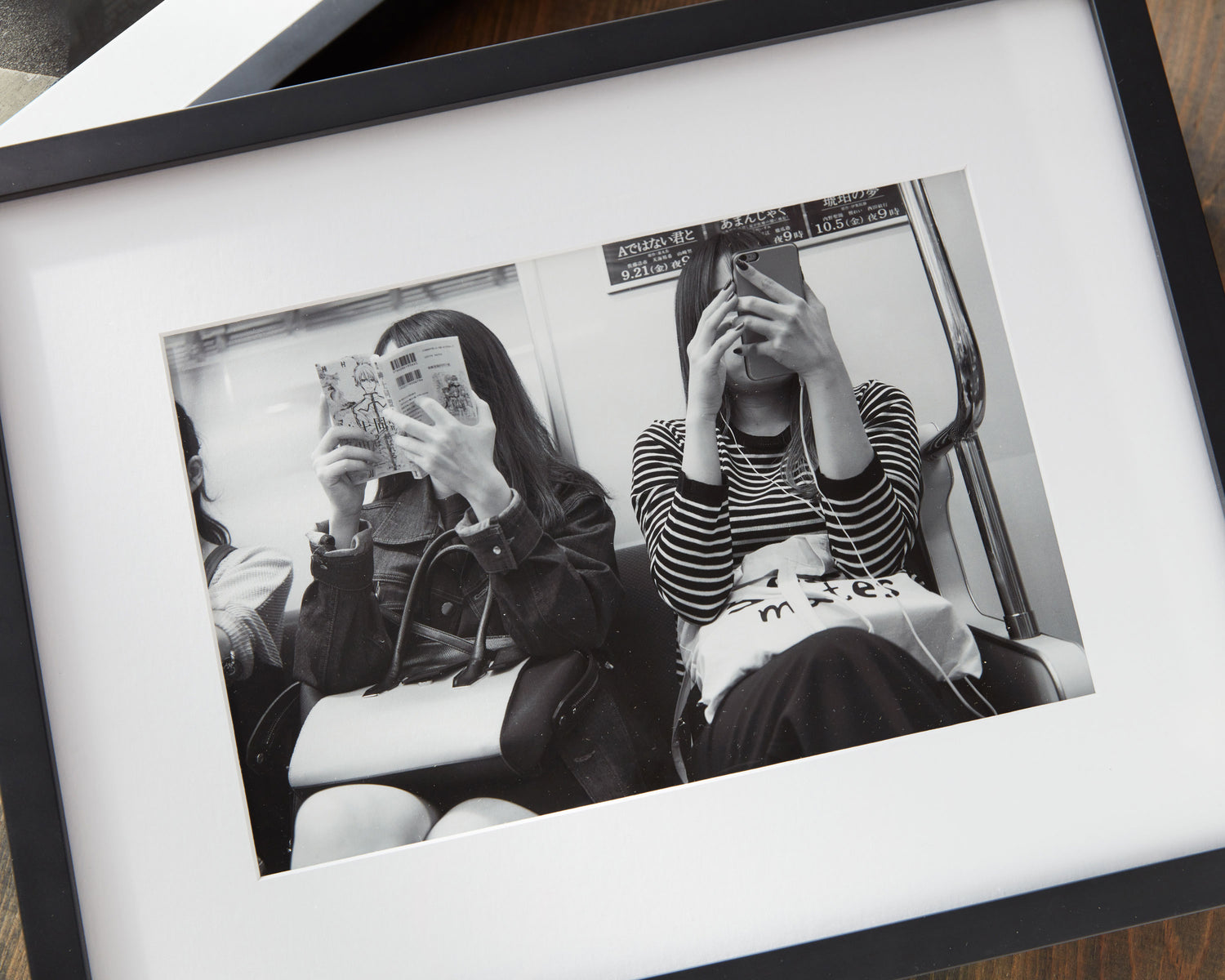 A black-framed black-and-white fine art photograph of two women on the Tokyo Metro, displayed on a dining room table, archival pigment print.