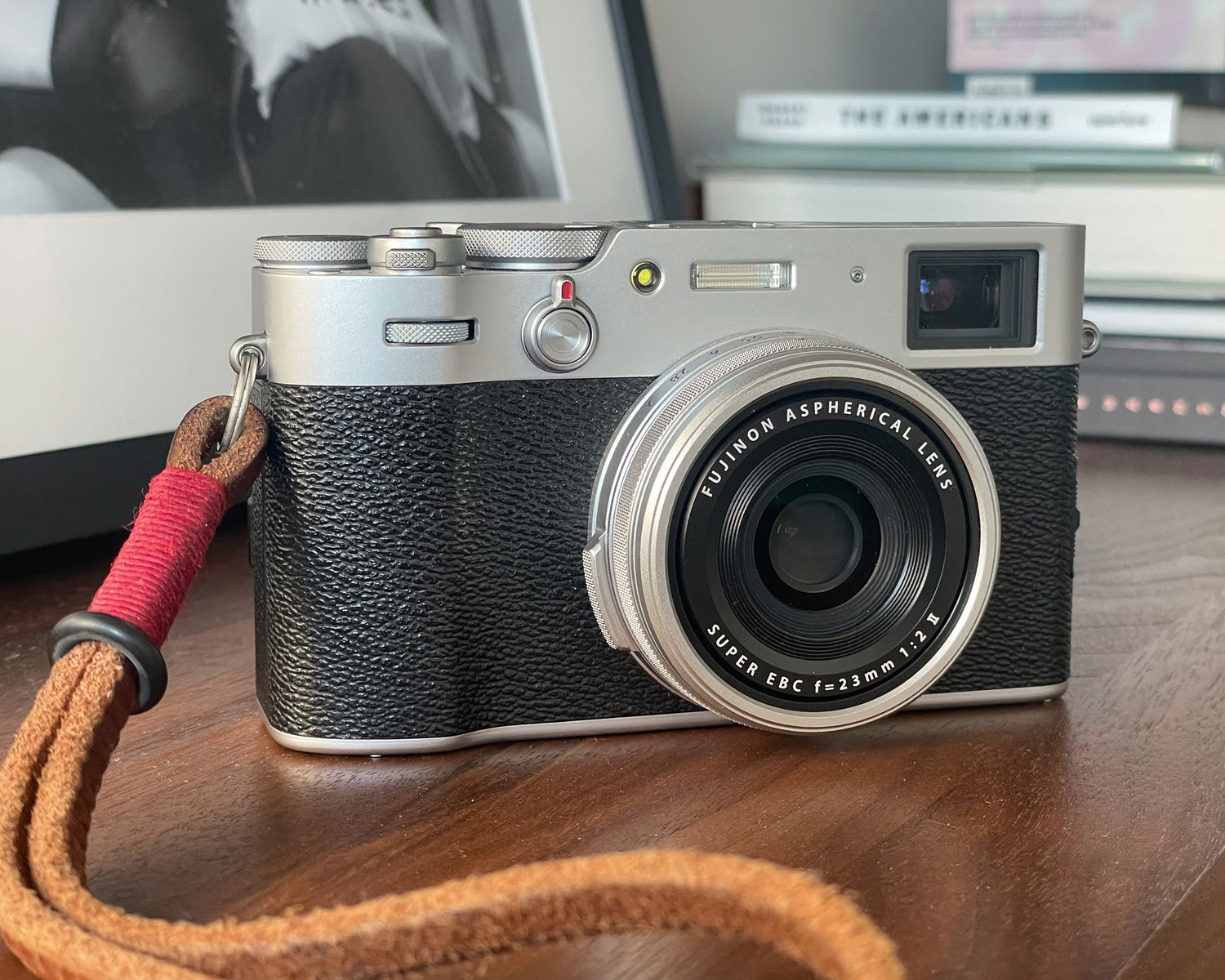 A rangefinder camera sitting on a bookshelf with a framed photograph and various photo books in the background.