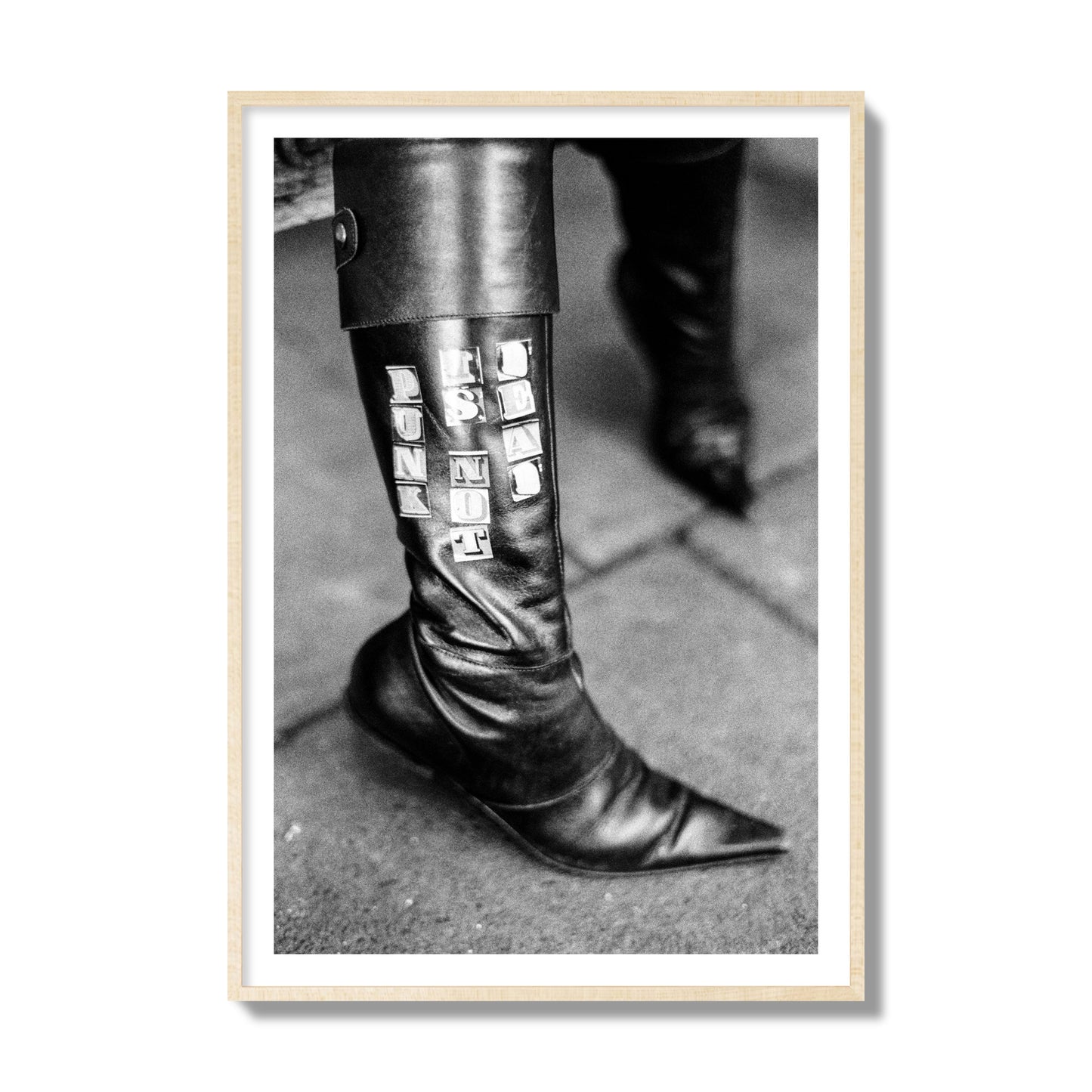 Fine art black and white photo of a woman's black leather boot with the words Punk is Not Dead, archival pigment print, collector size, natural wood frame.