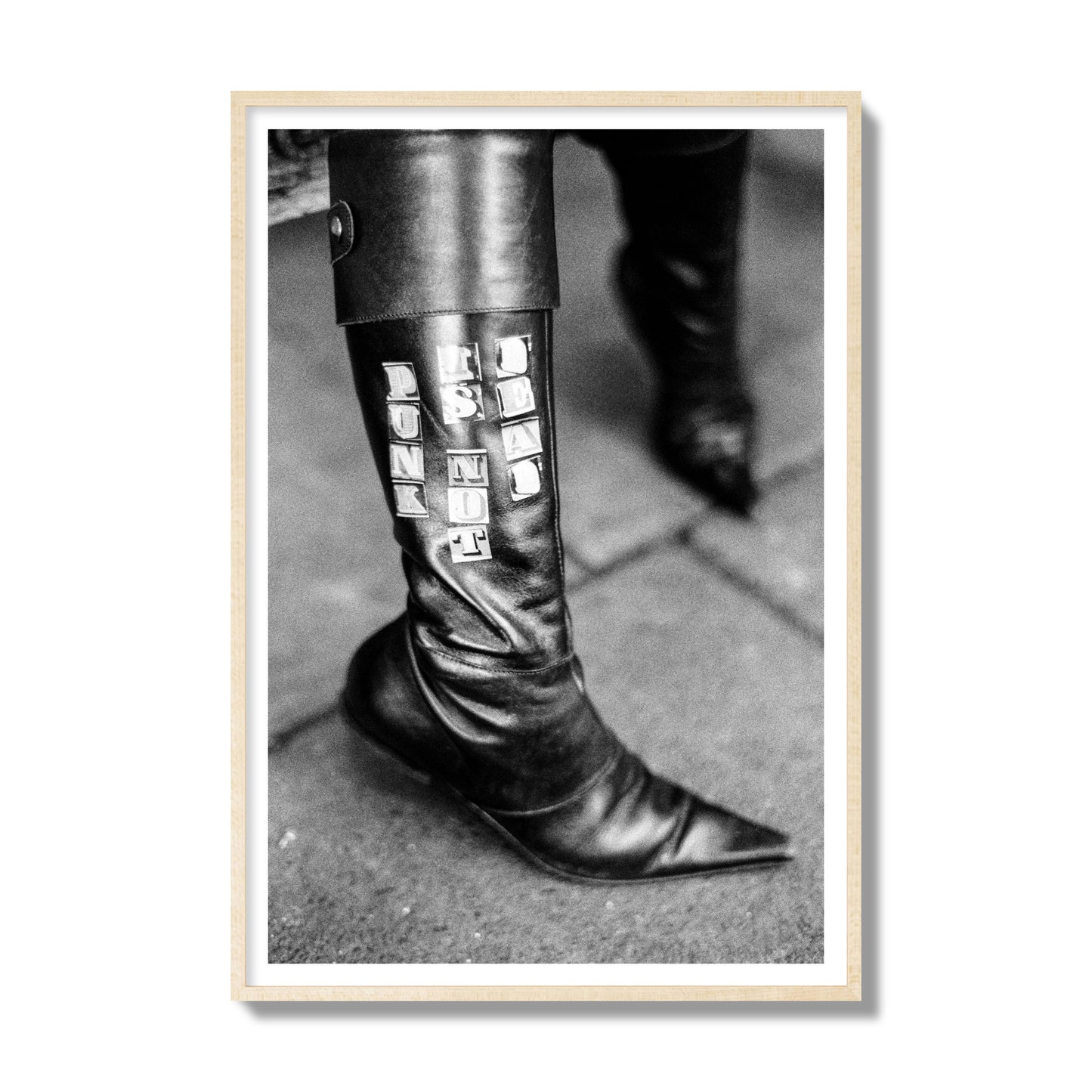 Fine art black and white photo of a woman's black leather boot with the words Punk is Not Dead, archival pigment print, gallery size, natural wood frame.