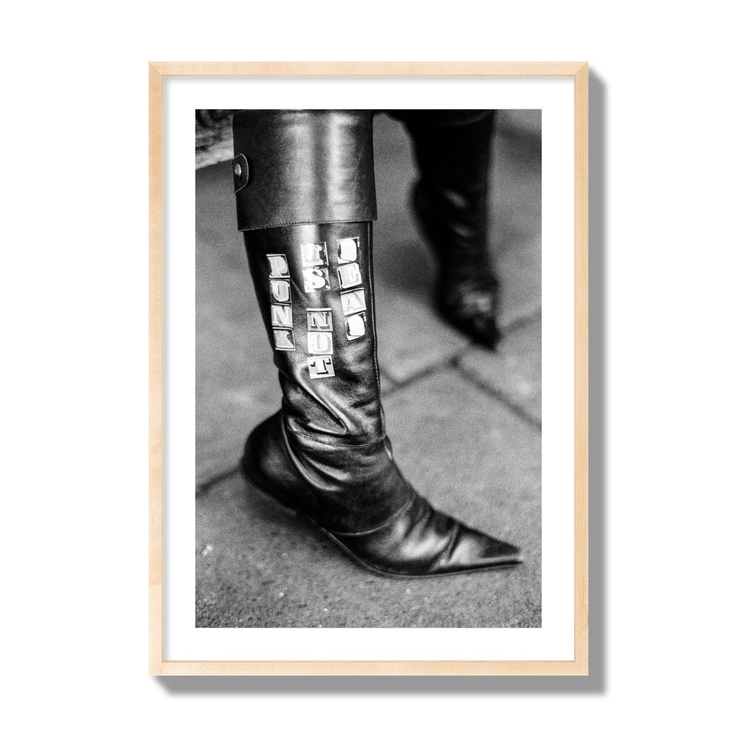 Fine art black and white photo of a woman's black leather boot with the words Punk is Not Dead, archival pigment print, giant size, natural wood frame.