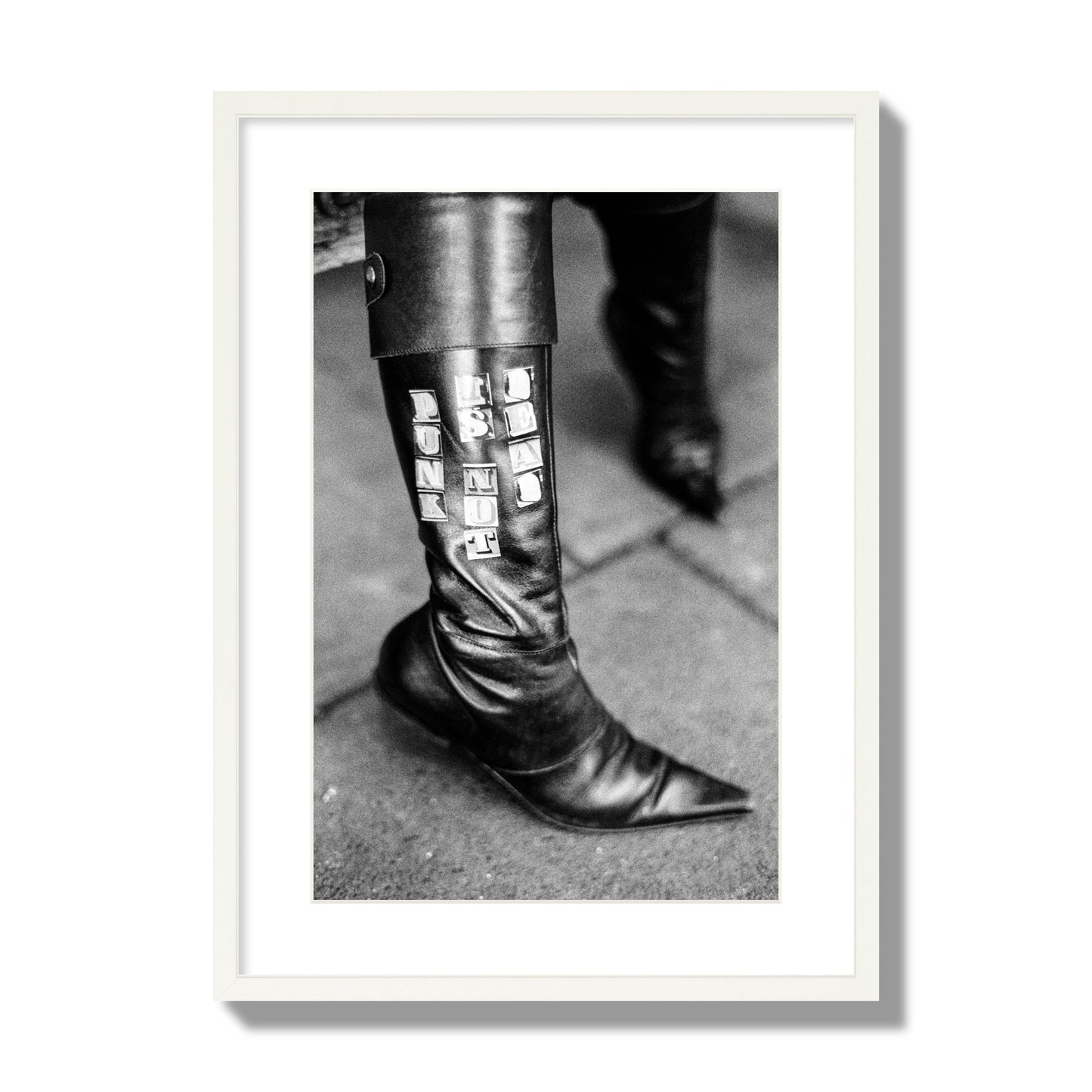 Fine art black and white photo of a woman's black leather boot with the words Punk is Not Dead, archival pigment print, large size, white frame.