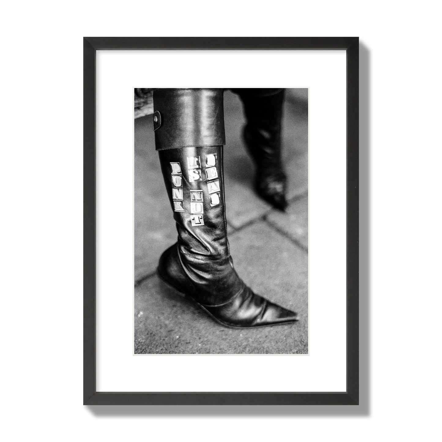 Fine art black and white photo of a woman's black leather boot with the words Punk is Not Dead, archival pigment print, medium size, black frame.