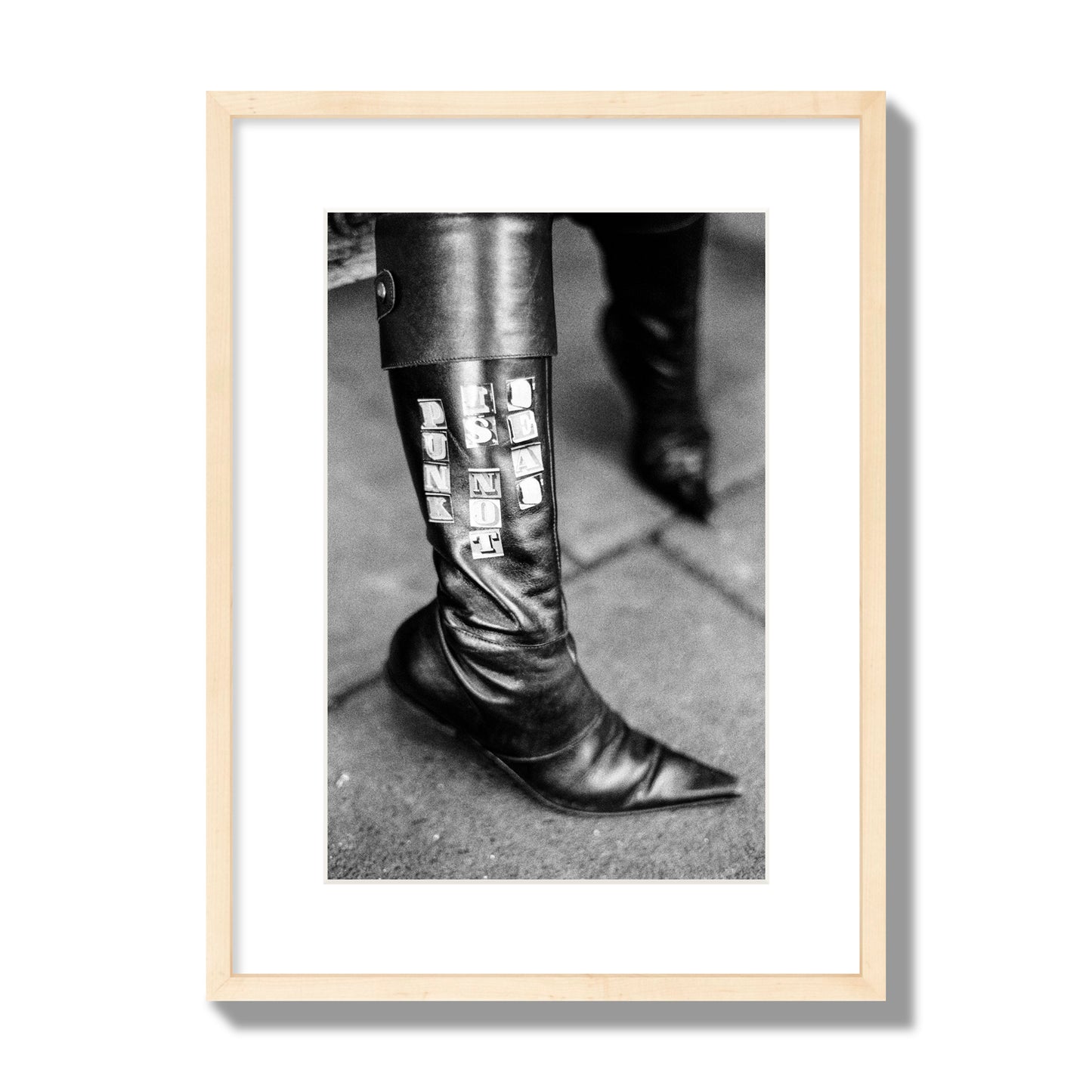 Fine art black and white photo of a woman's black leather boot with the words Punk is Not Dead, archival pigment print, medium size, natural wood frame.