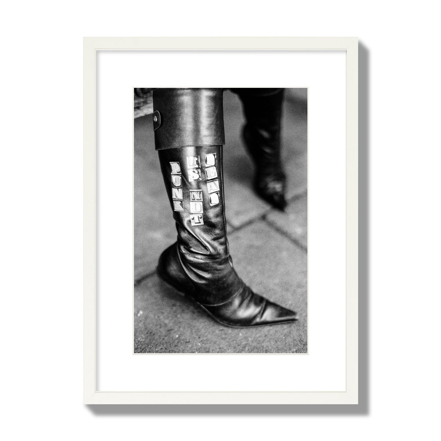 Fine art black and white photo of a woman's black leather boot with the words Punk is Not Dead, archival pigment print, medium size, white frame.