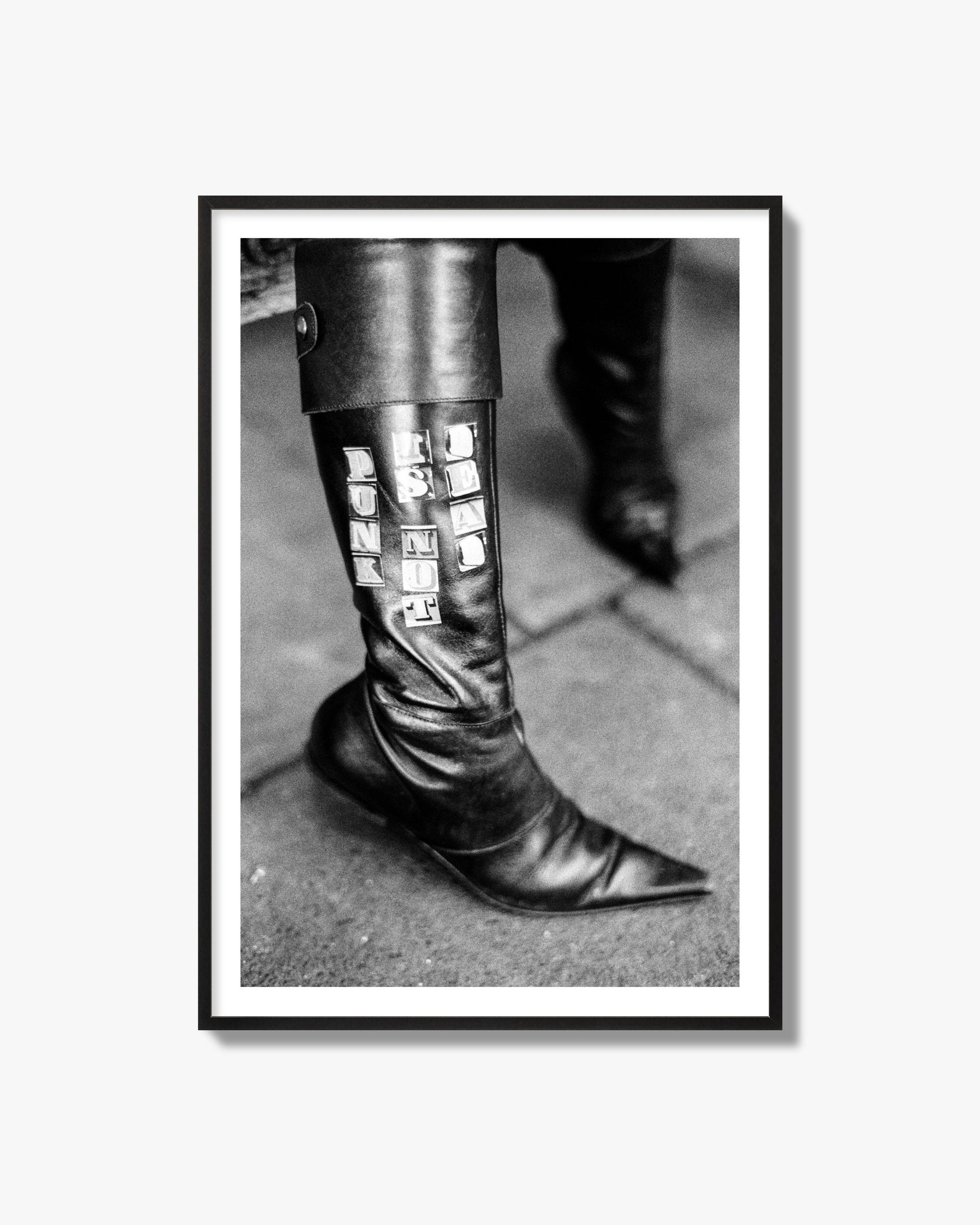 Fine art black and white photo of a woman's black leather boot with the words Punk is Not Dead, archival pigment print, black frame.