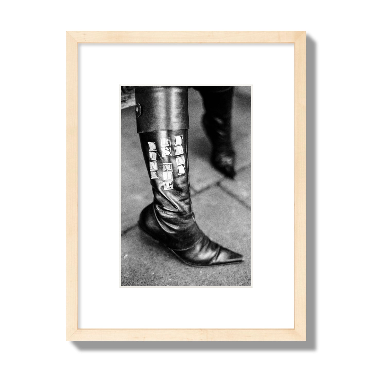 Fine art black and white photo of a woman's black leather boot with the words Punk is Not Dead, archival pigment print, small size, natural wood frame.