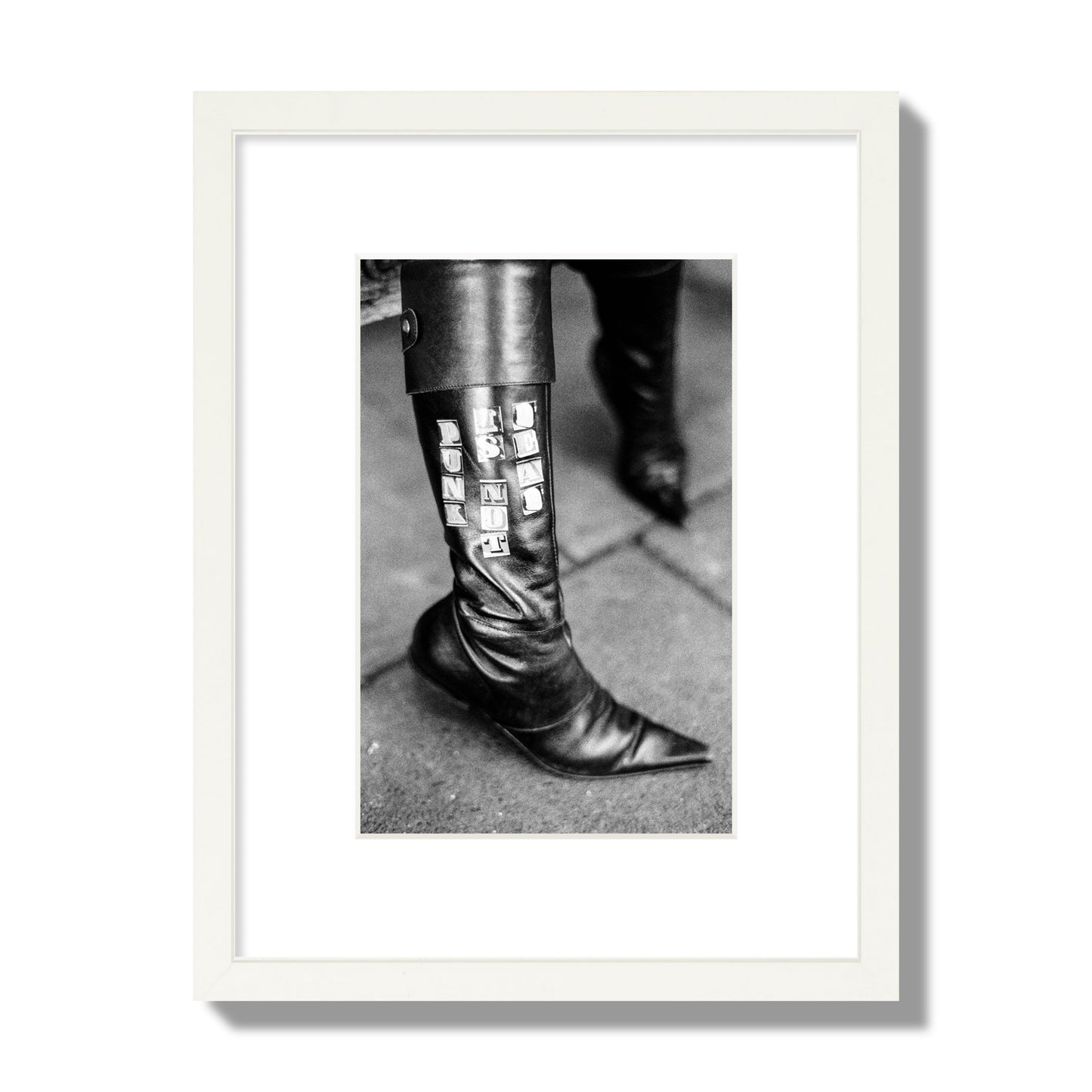Fine art black and white photo of a woman's black leather boot with the words Punk is Not Dead, archival pigment print, small size, white frame.