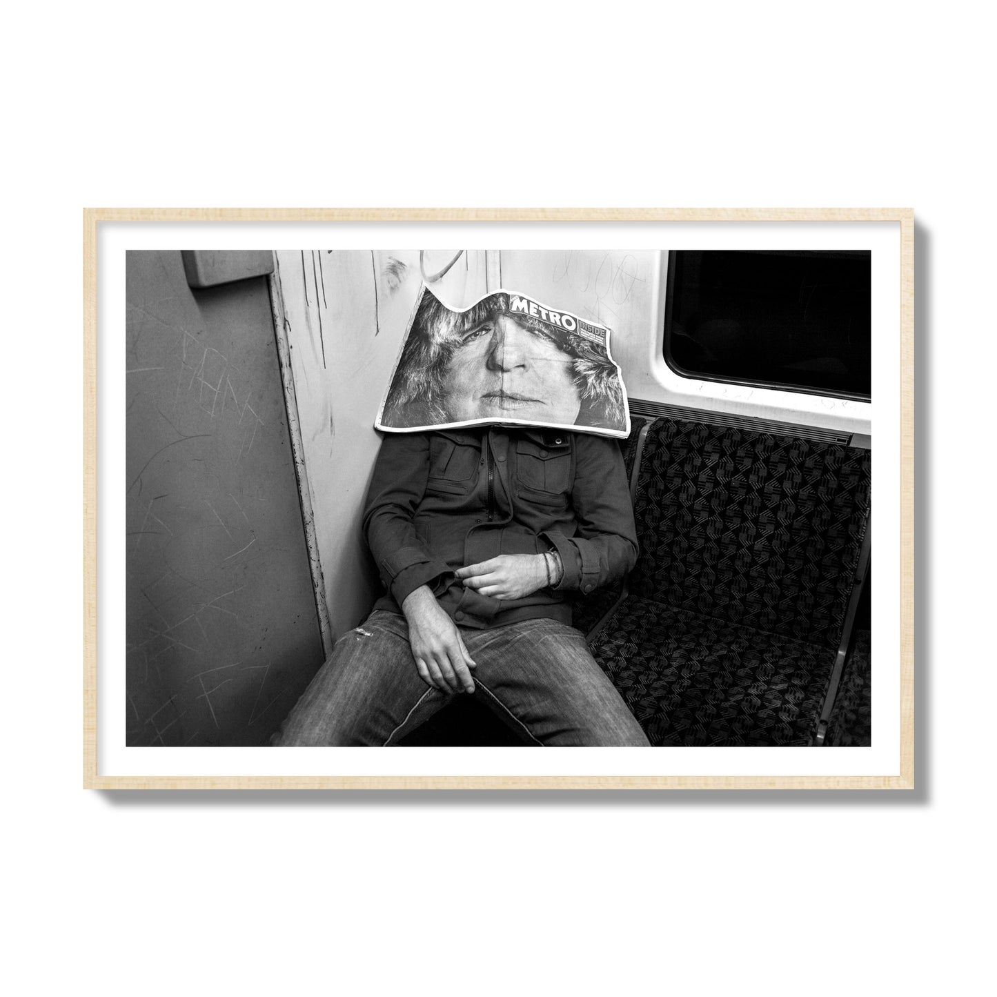 Fine art photograph of a man asleep on the subway with a newspaper covering their face, archival pigment print, collector size, natural wood frame.