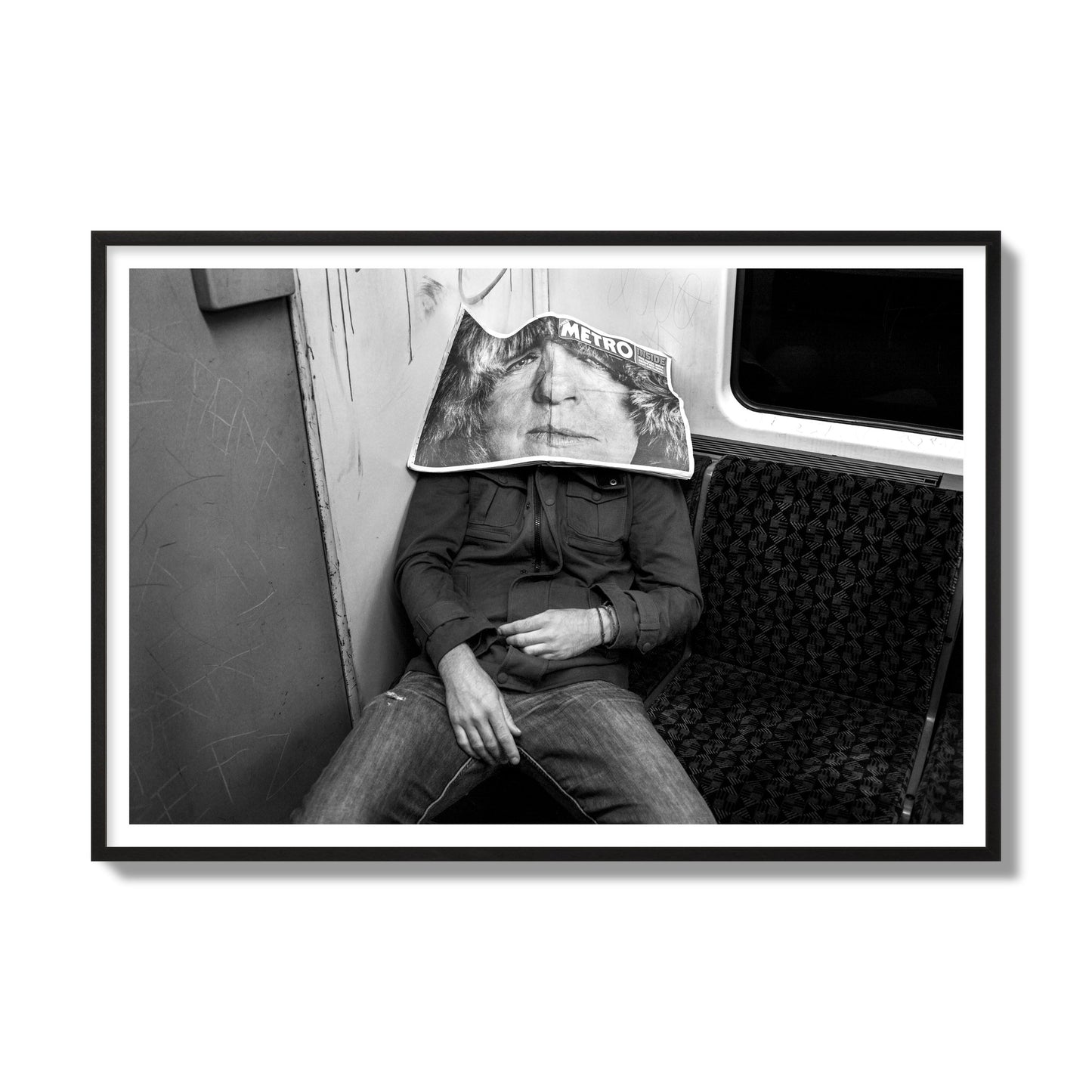 Fine art photograph of a man asleep on the subway with a newspaper covering their face, archival pigment print, gallery size, black frame.