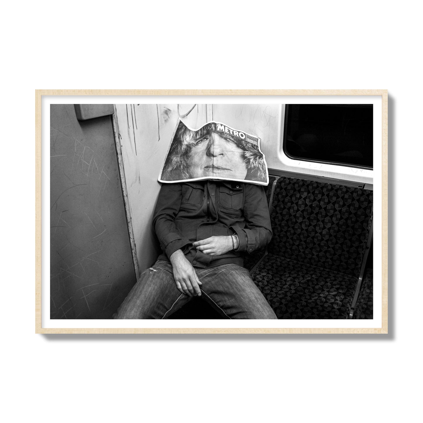 Fine art photograph of a man asleep on the subway with a newspaper covering their face, archival pigment print, gallery size, natural wood frame.