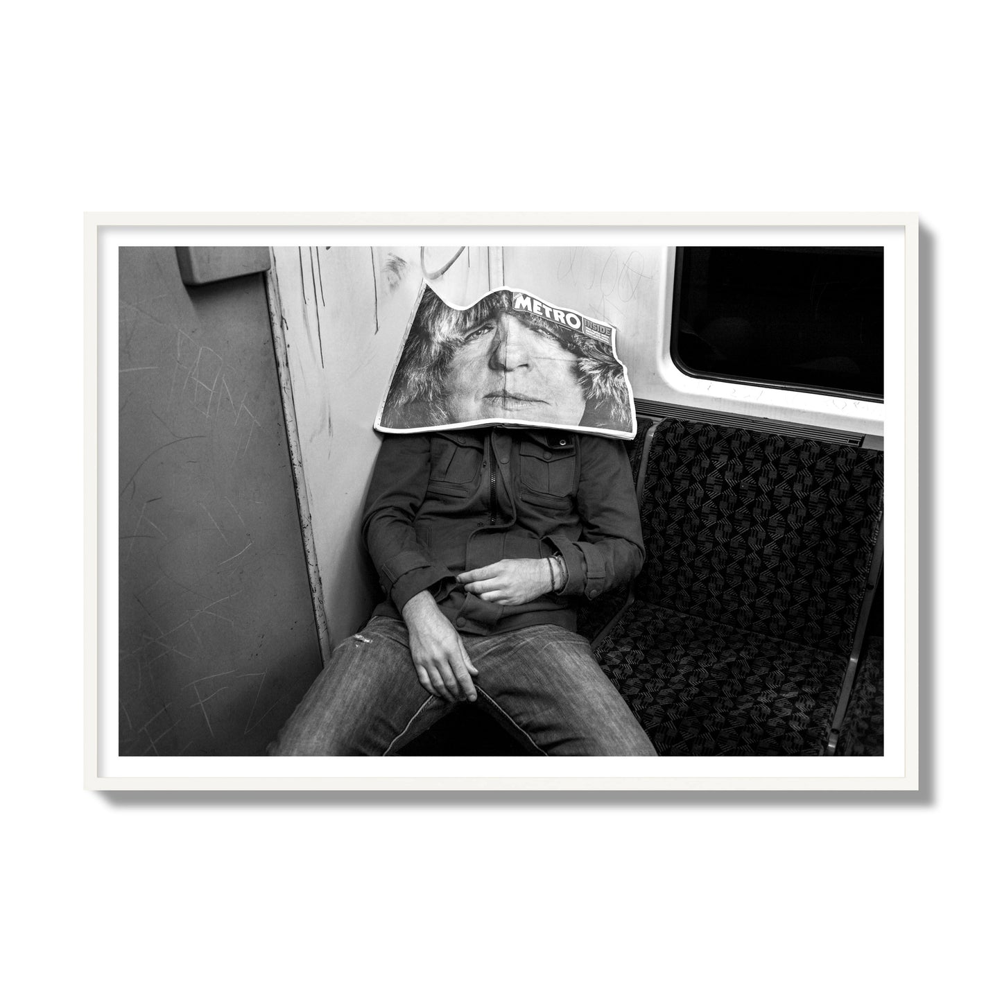 Fine art photograph of a man asleep on the subway with a newspaper covering their face, archival pigment print, gallery size, white frame.