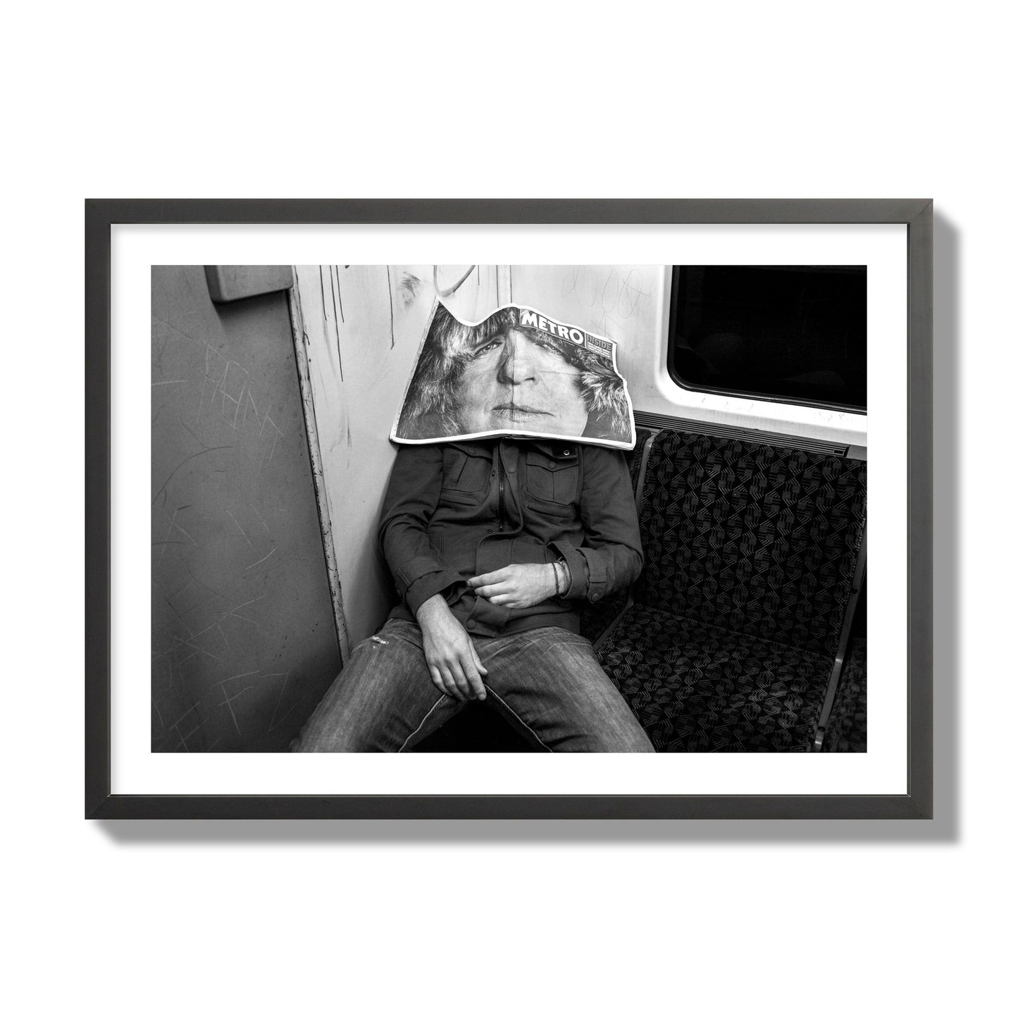 Fine art photograph of a man asleep on the subway with a newspaper covering their face, archival pigment print, giant size, black frame.