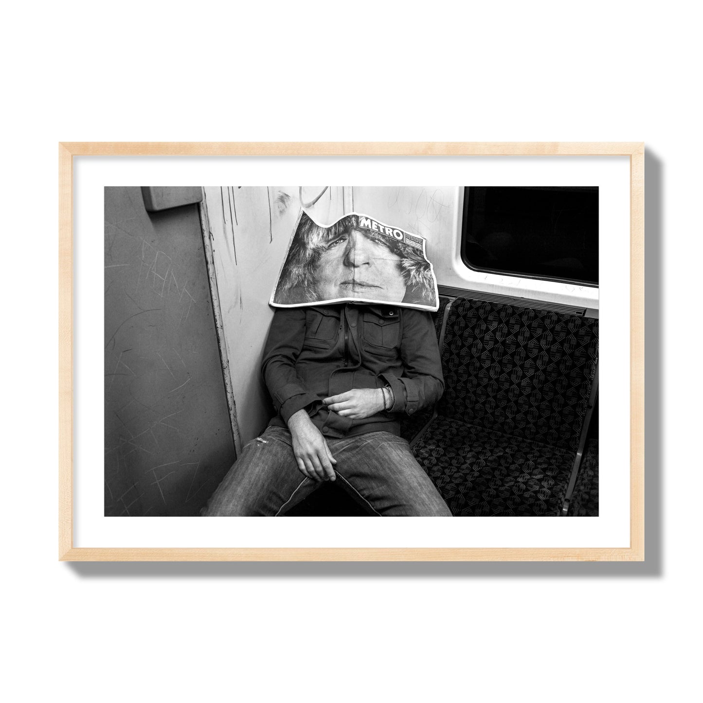 Fine art photograph of a man asleep on the subway with a newspaper covering their face, archival pigment print, giant size, natural wood frame.