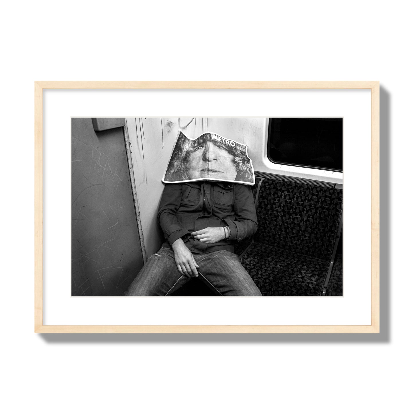Fine art photograph of a man asleep on the subway with a newspaper covering their face, archival pigment print, large size, natural wood frame.