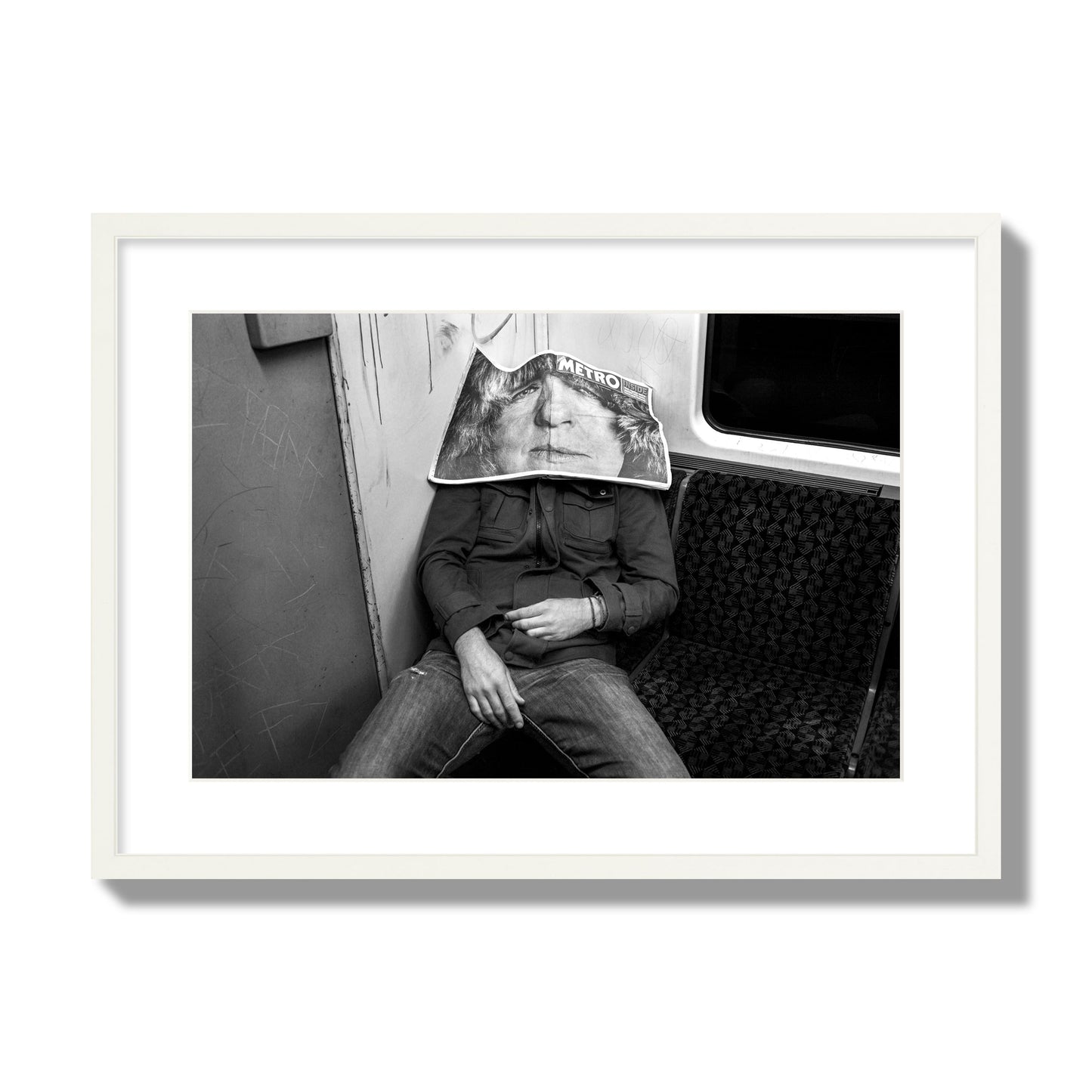 Fine art photograph of a man asleep on the subway with a newspaper covering their face, archival pigment print, large size, white frame.