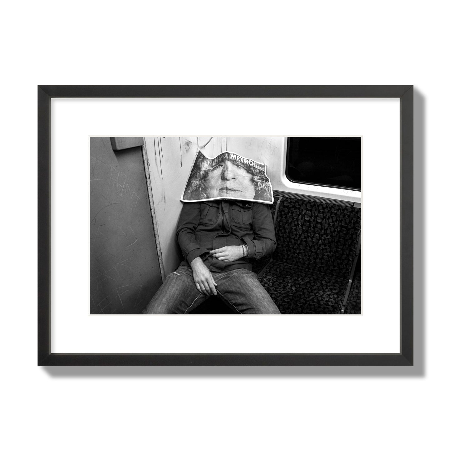 Fine art photograph of a man asleep on the subway with a newspaper covering their face, archival pigment print, medium size, black frame.