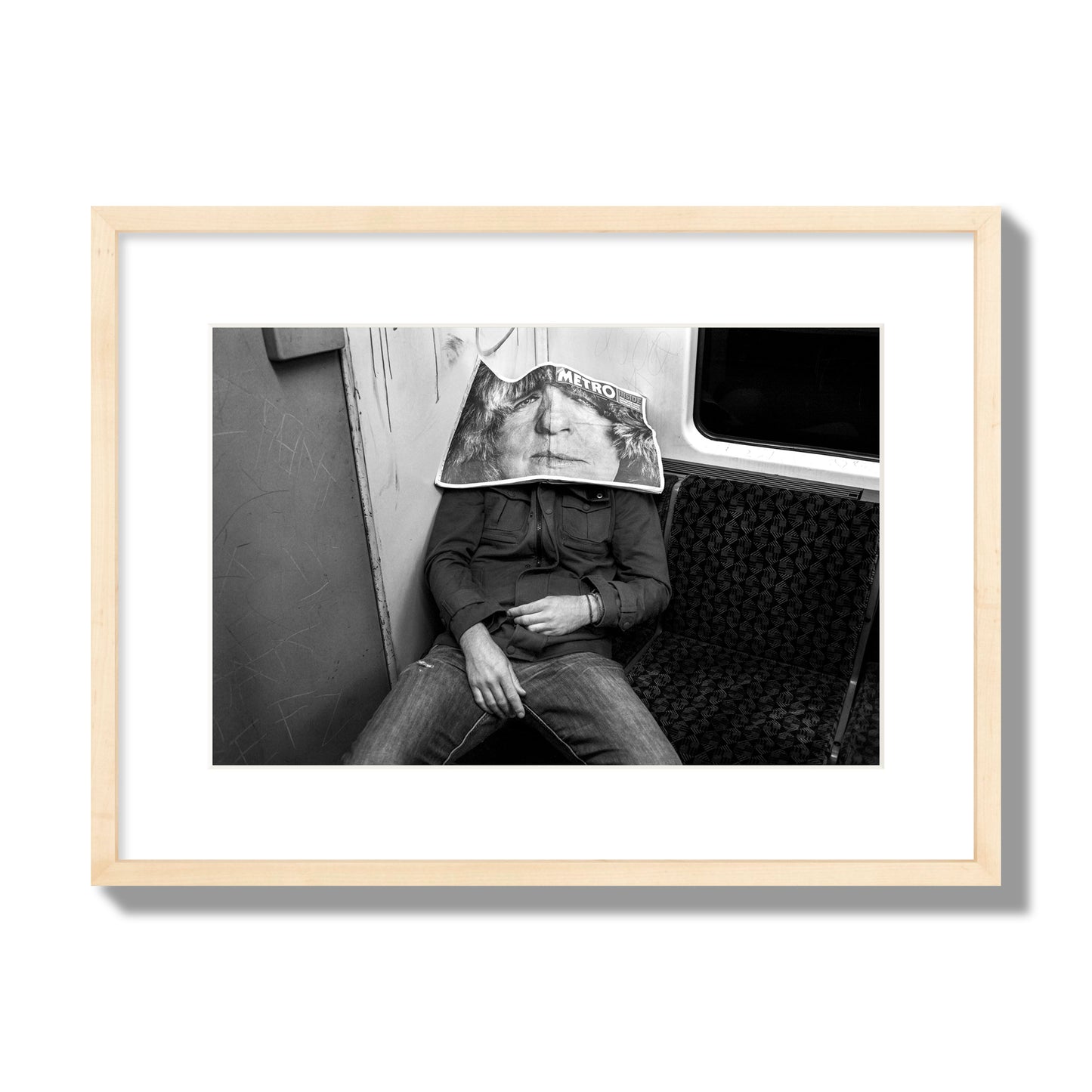 Fine art photograph of a man asleep on the subway with a newspaper covering their face, archival pigment print, medium size, natural wood frame.
