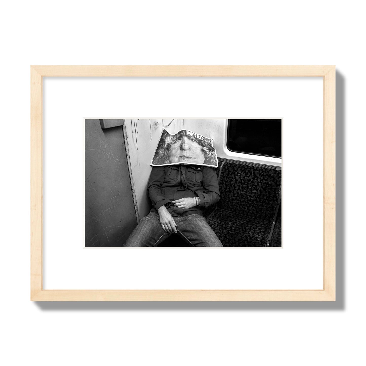 Fine art photograph of a man asleep on the subway with a newspaper covering their face, archival pigment print, small size, natural wood frame.