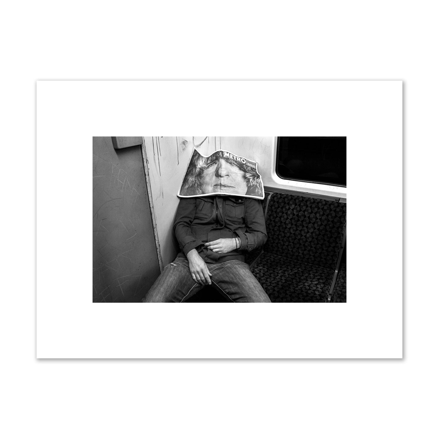 Fine art photograph of a man asleep on the subway with a newspaper covering their face, archival pigment print, small size, unframed.
