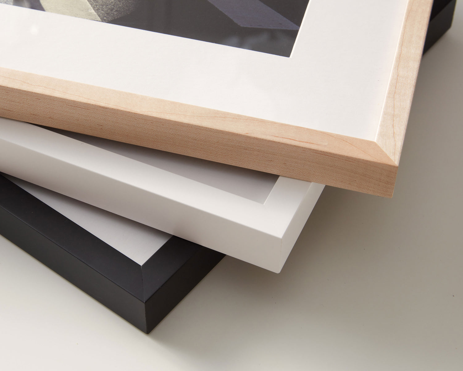 Three archival pigment prints, each framed in a different color — black, white, and natural wood — stacked on top of each other to showcase the high-end hardwood frames.