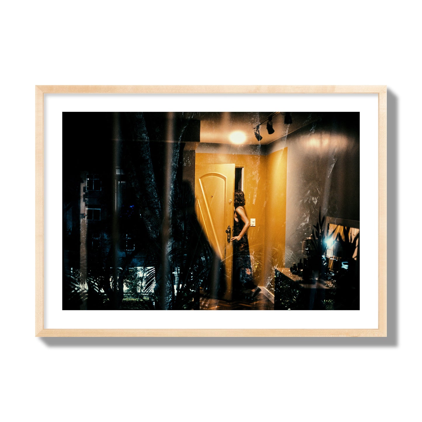 Fine art street photograph of a woman opening a bright yellow door to her living room, with reflections of the outside environment layered over the scene. Archival pigment print, giant size, natural wood frame.