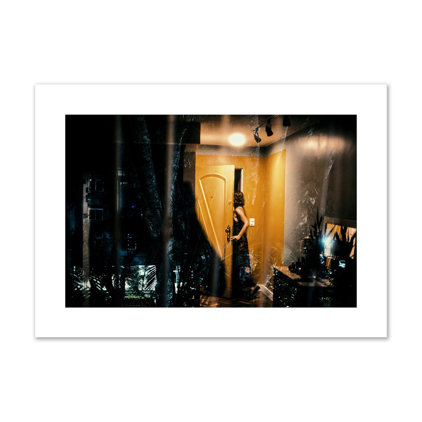 Fine art street photograph of a woman opening a bright yellow door to her living room, with reflections of the outside environment layered over the scene. Archival pigment print, giant size, unframed.