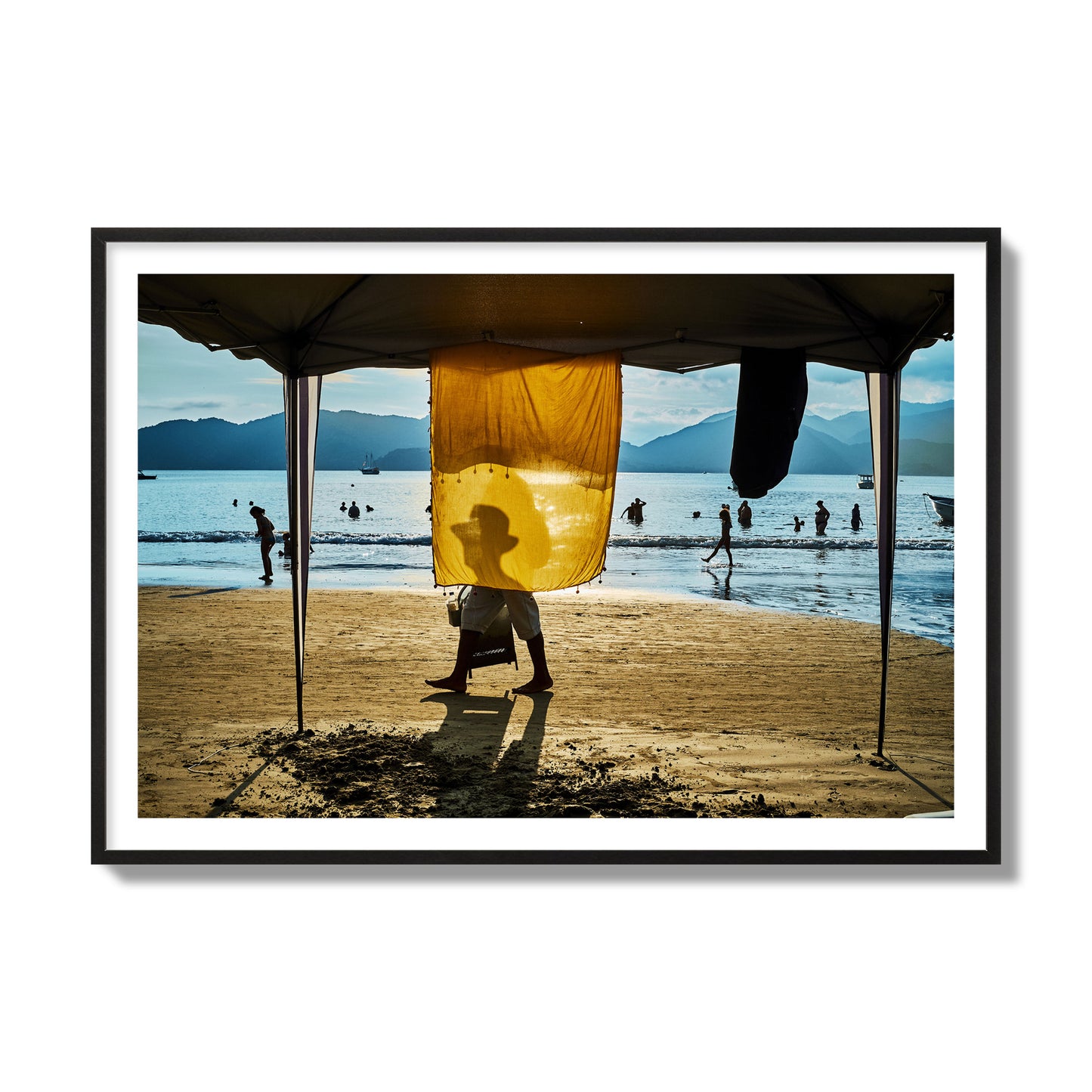 Fine art street photograph of a crowded beach scene with a vibrant yellow flap hanging from a tent, sunlight filtering through and silhouetting a man’s face. Archival pigment print, collector size, black frame.