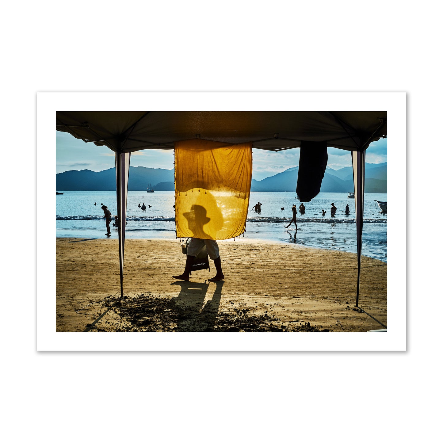 Fine art street photograph of a crowded beach scene with a vibrant yellow flap hanging from a tent, sunlight filtering through and silhouetting a man’s face. Archival pigment print, collector size, unframed.