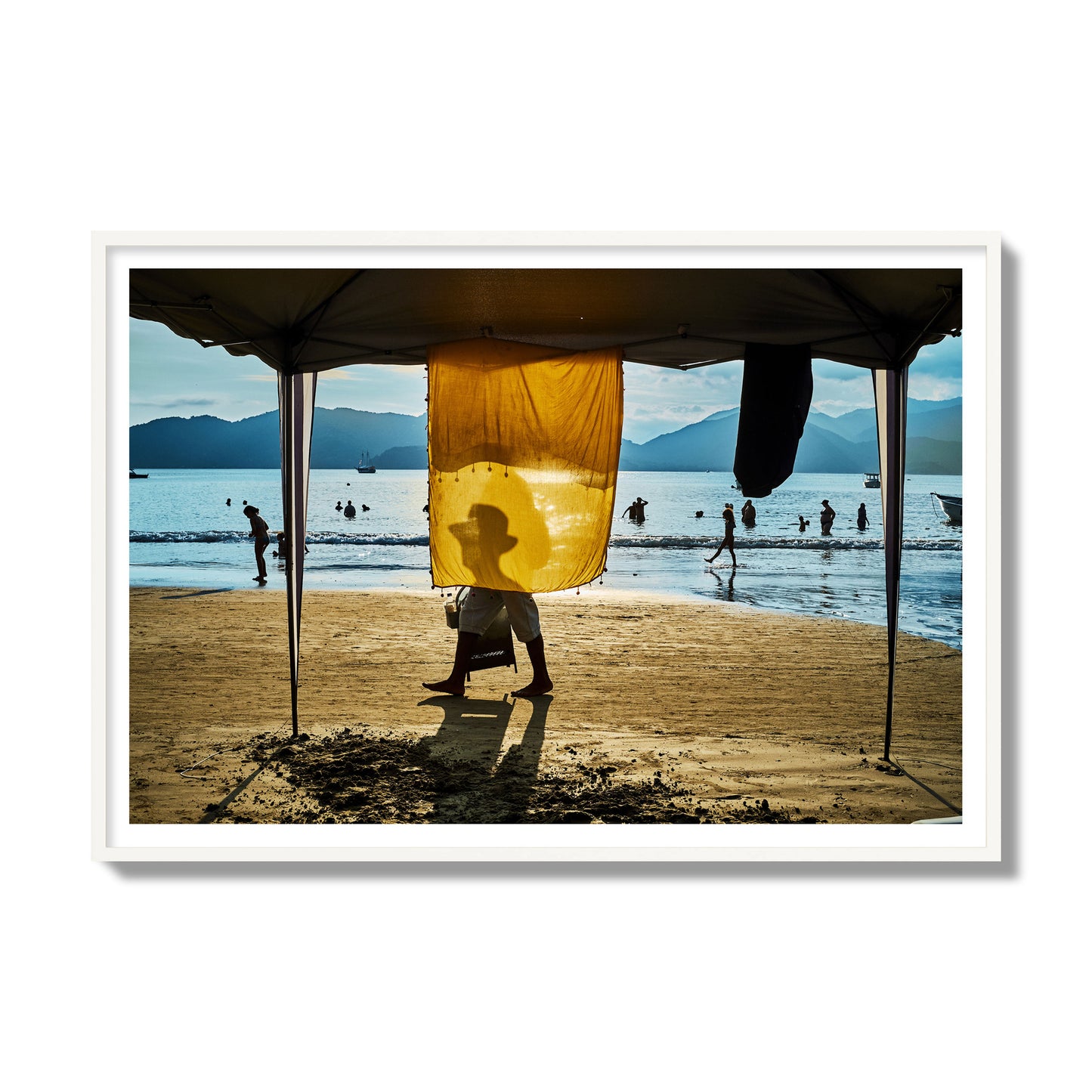 Fine art street photograph of a crowded beach scene with a vibrant yellow flap hanging from a tent, sunlight filtering through and silhouetting a man’s face. Archival pigment print, gallery size, white frame.