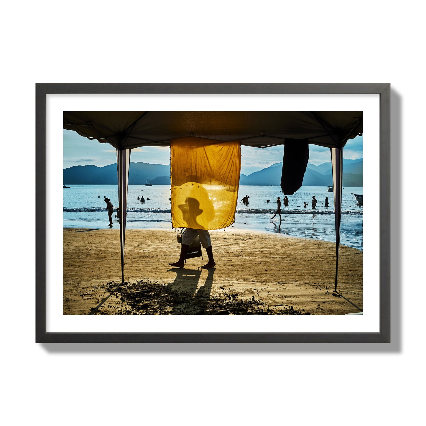 Fine art street photograph of a crowded beach scene with a vibrant yellow flap hanging from a tent, sunlight filtering through and silhouetting a man’s face. Archival pigment print, giant size, black frame.