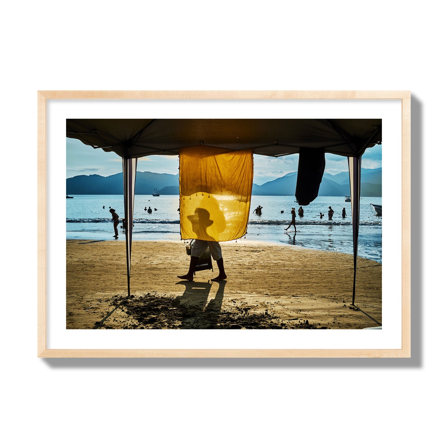 Fine art street photograph of a crowded beach scene with a vibrant yellow flap hanging from a tent, sunlight filtering through and silhouetting a man’s face. Archival pigment print, giant size, natural wood frame.