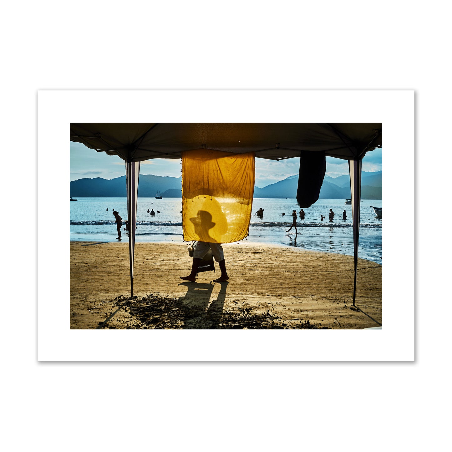 Fine art street photograph of a crowded beach scene with a vibrant yellow flap hanging from a tent, sunlight filtering through and silhouetting a man’s face. Archival pigment print, giant size, unframed.