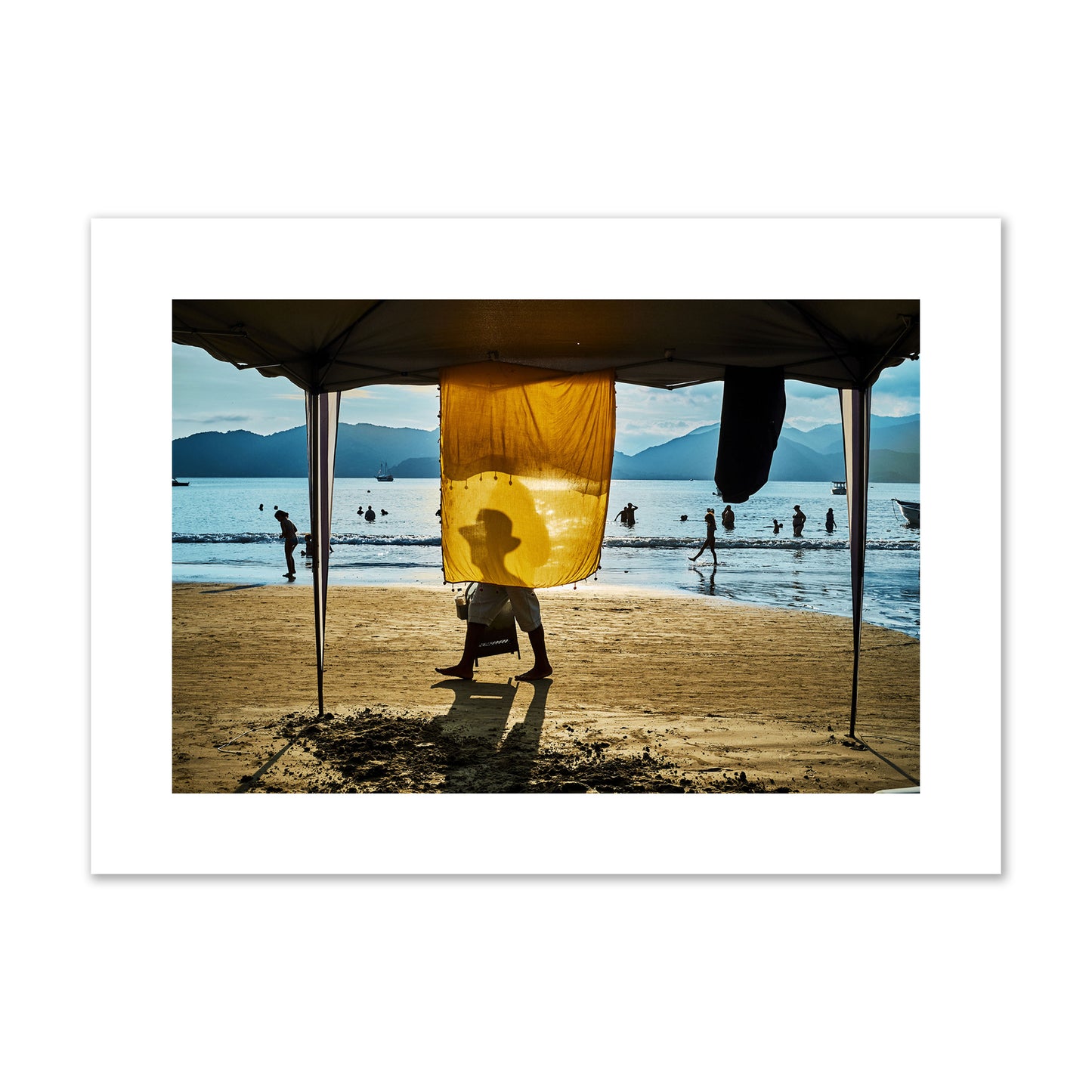 Fine art street photograph of a crowded beach scene with a vibrant yellow flap hanging from a tent, sunlight filtering through and silhouetting a man’s face. Archival pigment print, large size, unframed.