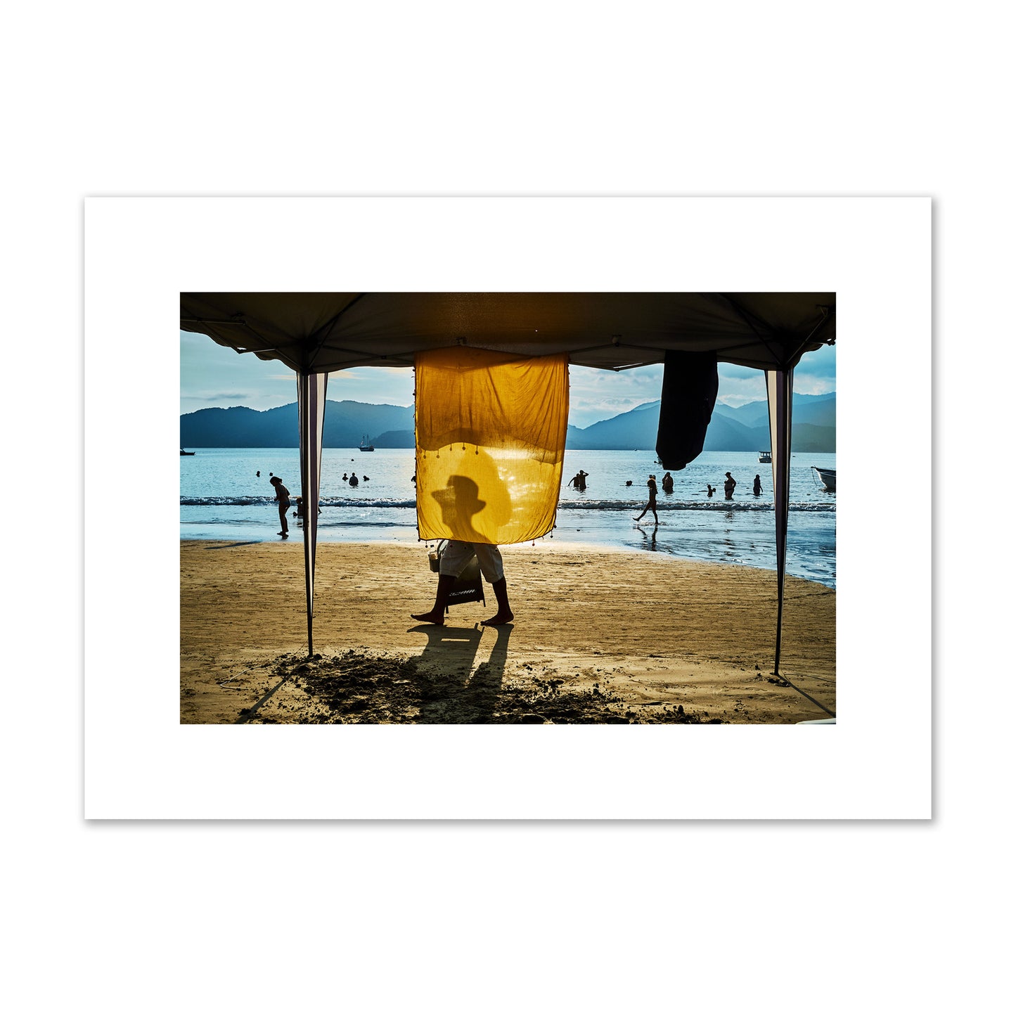 Fine art street photograph of a crowded beach scene with a vibrant yellow flap hanging from a tent, sunlight filtering through and silhouetting a man’s face. Archival pigment print, medium size, unframed.