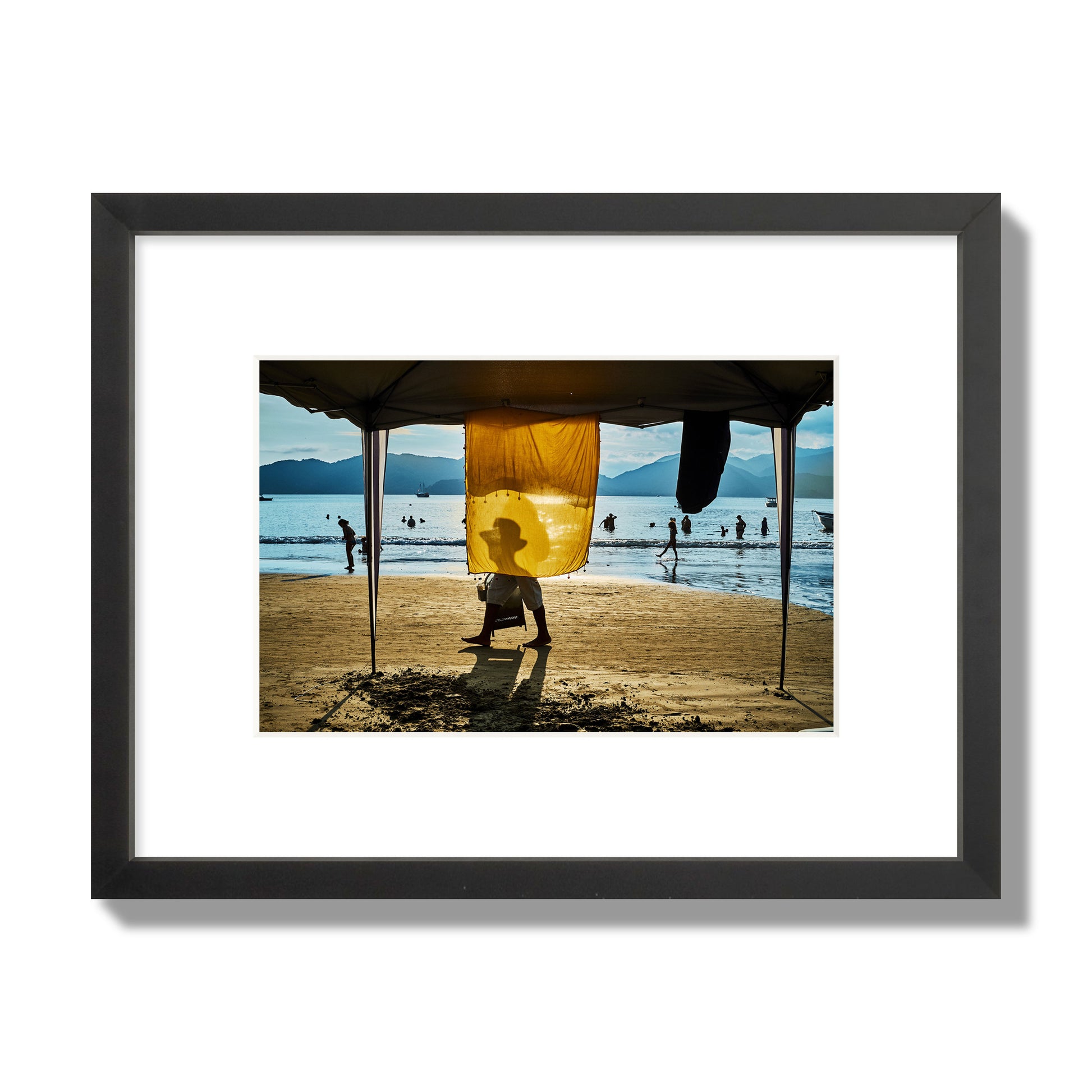 Fine art street photograph of a crowded beach scene with a vibrant yellow flap hanging from a tent, sunlight filtering through and silhouetting a man’s face. Archival pigment print, small size, black frame.
