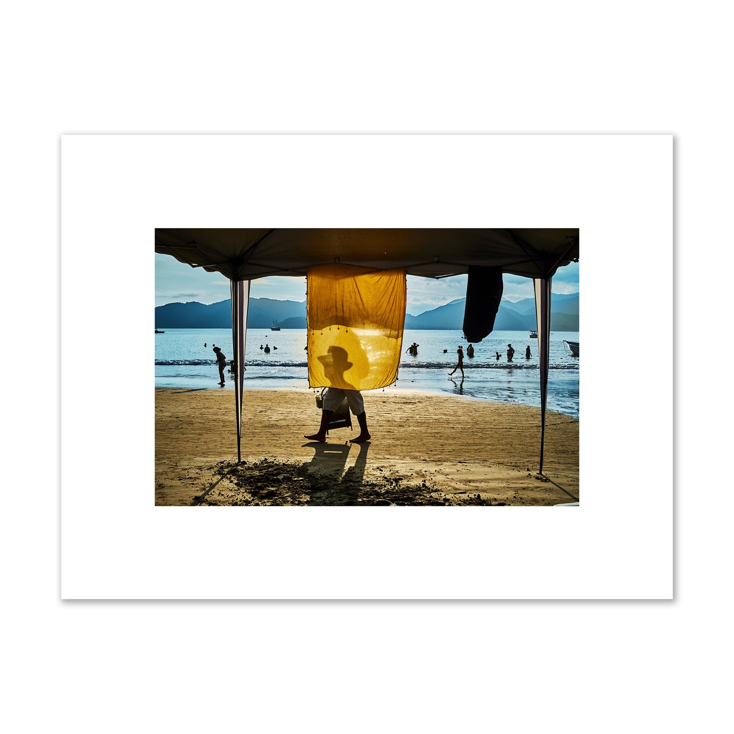 Fine art street photograph of a crowded beach scene with a vibrant yellow flap hanging from a tent, sunlight filtering through and silhouetting a man’s face. Archival pigment print, small size, unframed.