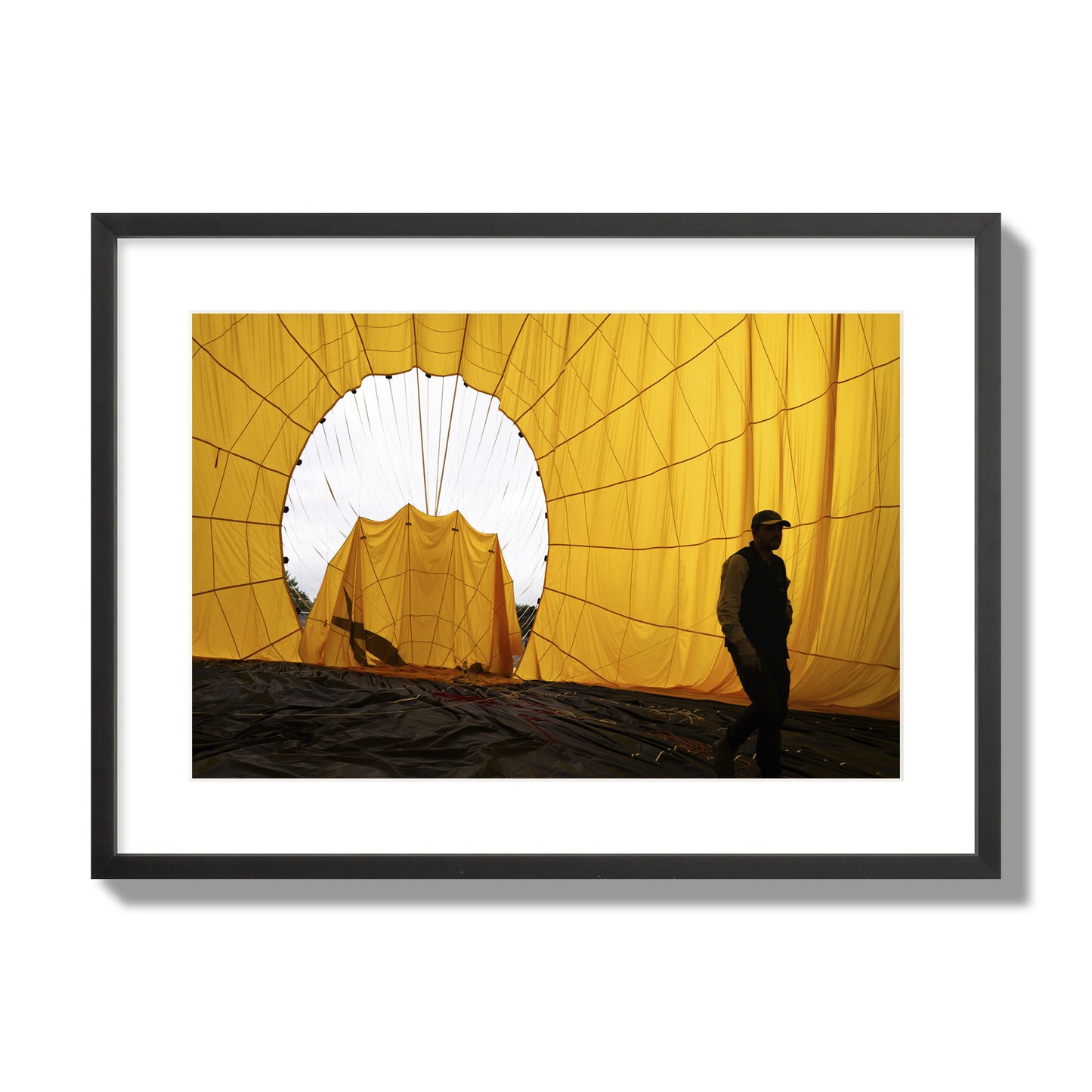 Fine art photograph of a man walking inside a bright yellow hot air balloon as it slowly deflates. Archival pigment print, large size, black frame.