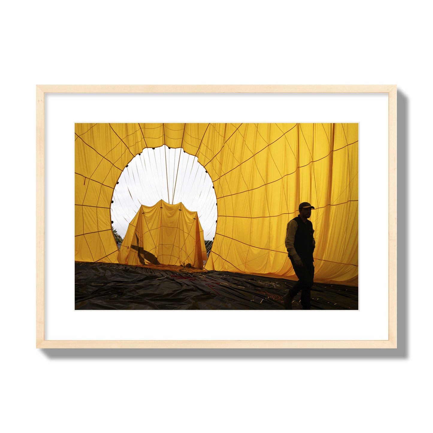Fine art photograph of a man walking inside a bright yellow hot air balloon as it slowly deflates. Archival pigment print, large size, natural wood frame.