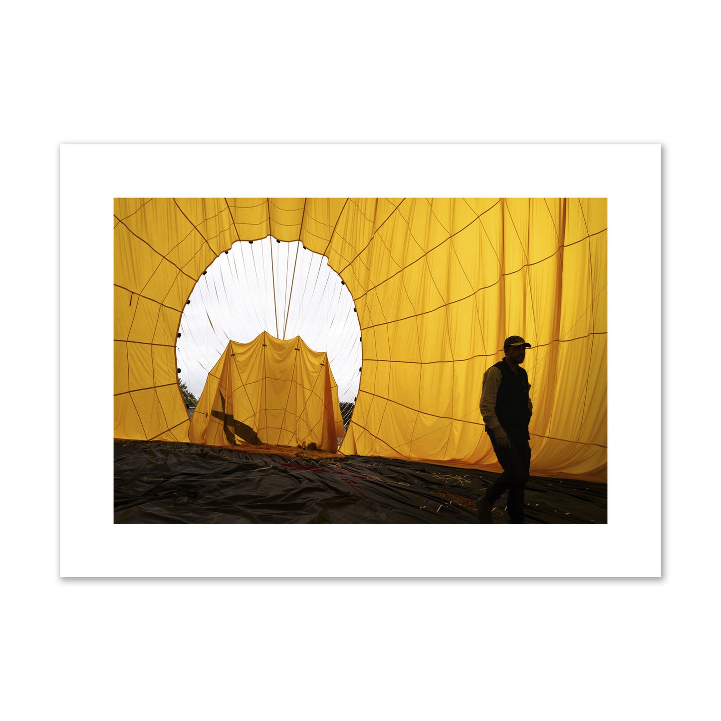Fine art photograph of a man walking inside a bright yellow hot air balloon as it slowly deflates. Archival pigment print, large size, unframed.