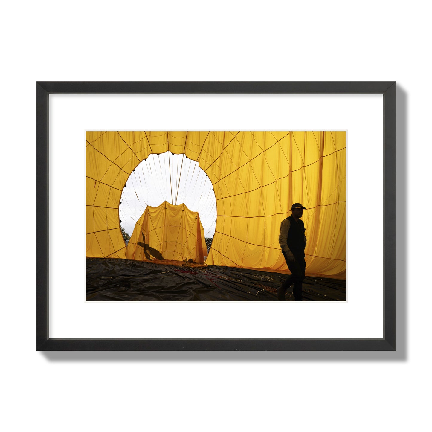 Fine art photograph of a man walking inside a bright yellow hot air balloon as it slowly deflates. Archival pigment print, medium size, black frame.