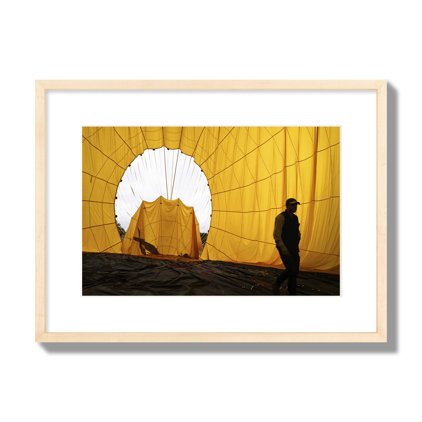 Fine art photograph of a man walking inside a bright yellow hot air balloon as it slowly deflates. Archival pigment print, medium size, natural wood frame.