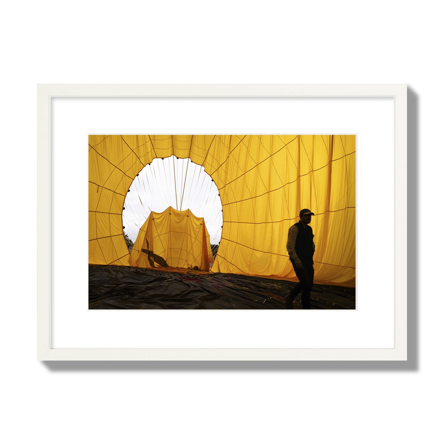 Fine art photograph of a man walking inside a bright yellow hot air balloon as it slowly deflates. Archival pigment print, medium size, white frame.