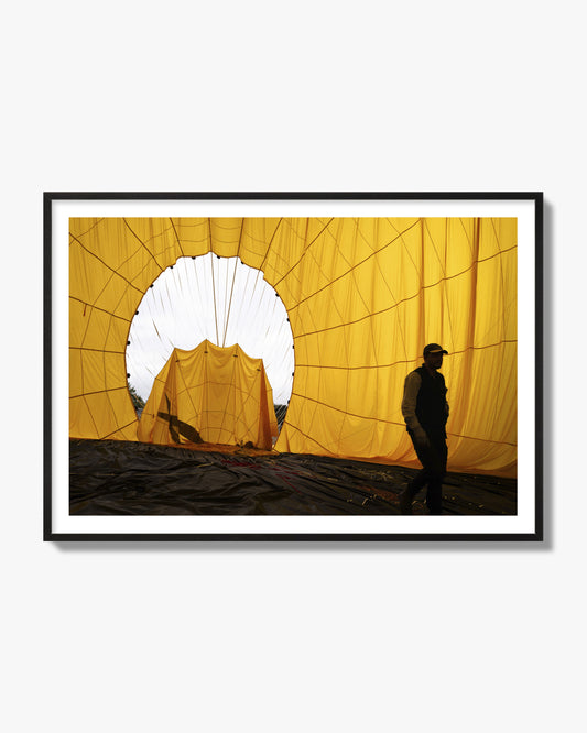 Fine art photograph of a man walking inside a bright yellow hot air balloon as it slowly deflates. Archival pigment print, black frame.