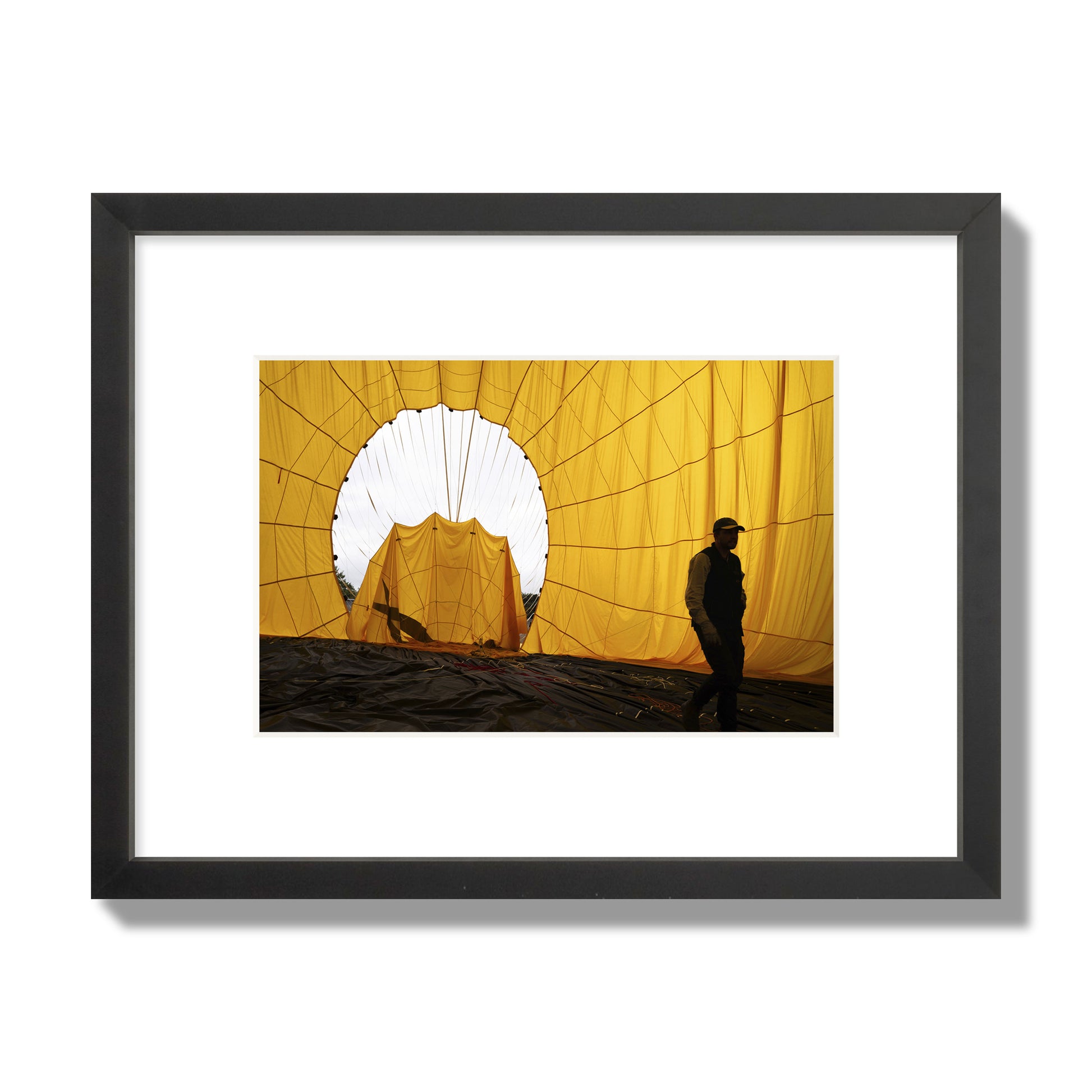 Fine art photograph of a man walking inside a bright yellow hot air balloon as it slowly deflates. Archival pigment print, small size, black frame.
