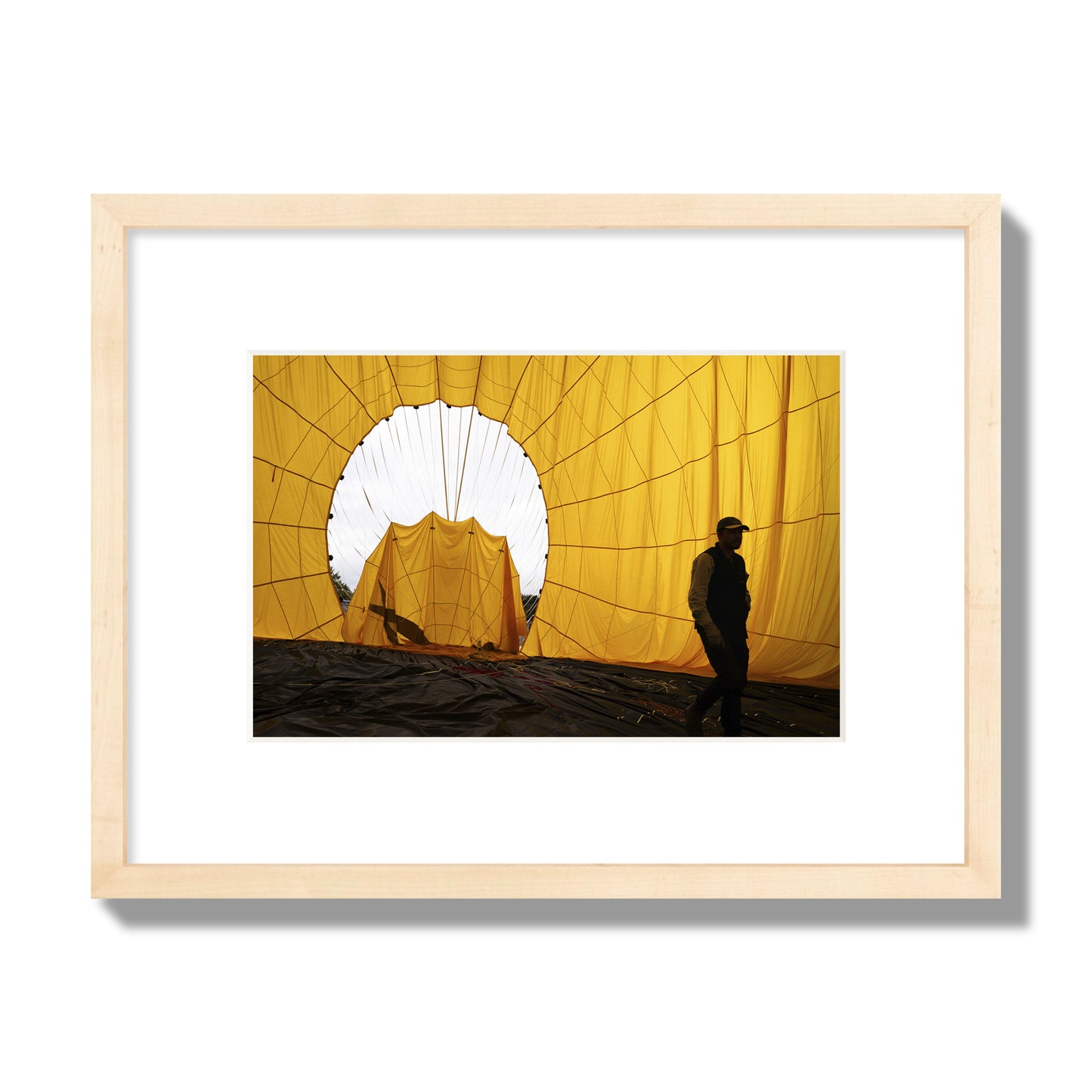 Fine art photograph of a man walking inside a bright yellow hot air balloon as it slowly deflates. Archival pigment print, small size, natural wood frame.