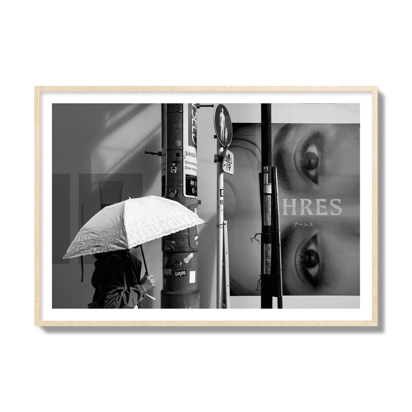Fine art street photograph of a woman walking with an umbrella on a Tokyo street, passing beneath a billboard with two large eyes. Archival pigment print, collector size, natural wood frame.