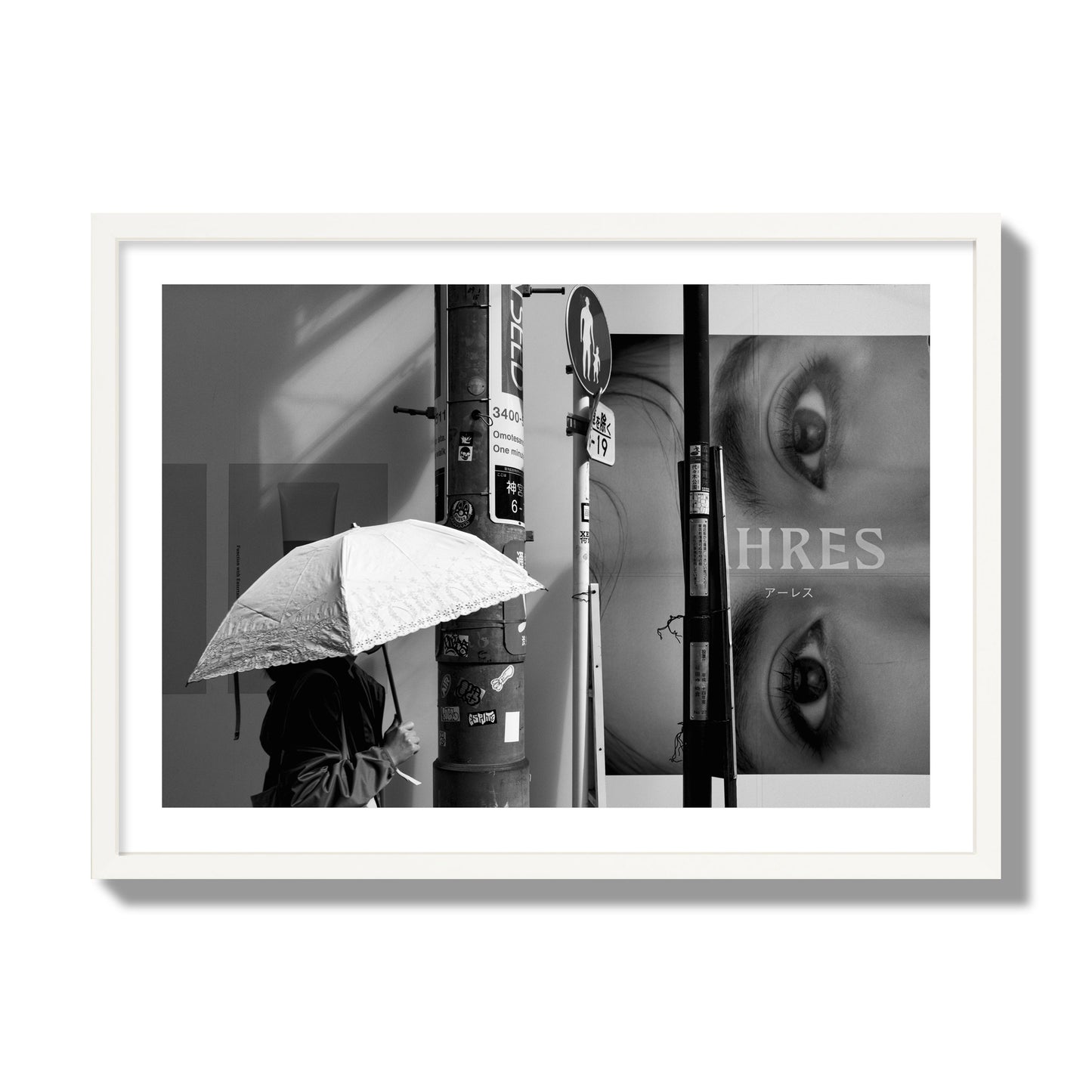 Fine art street photograph of a woman walking with an umbrella on a Tokyo street, passing beneath a billboard with two large eyes. Archival pigment print, giant size, white frame.