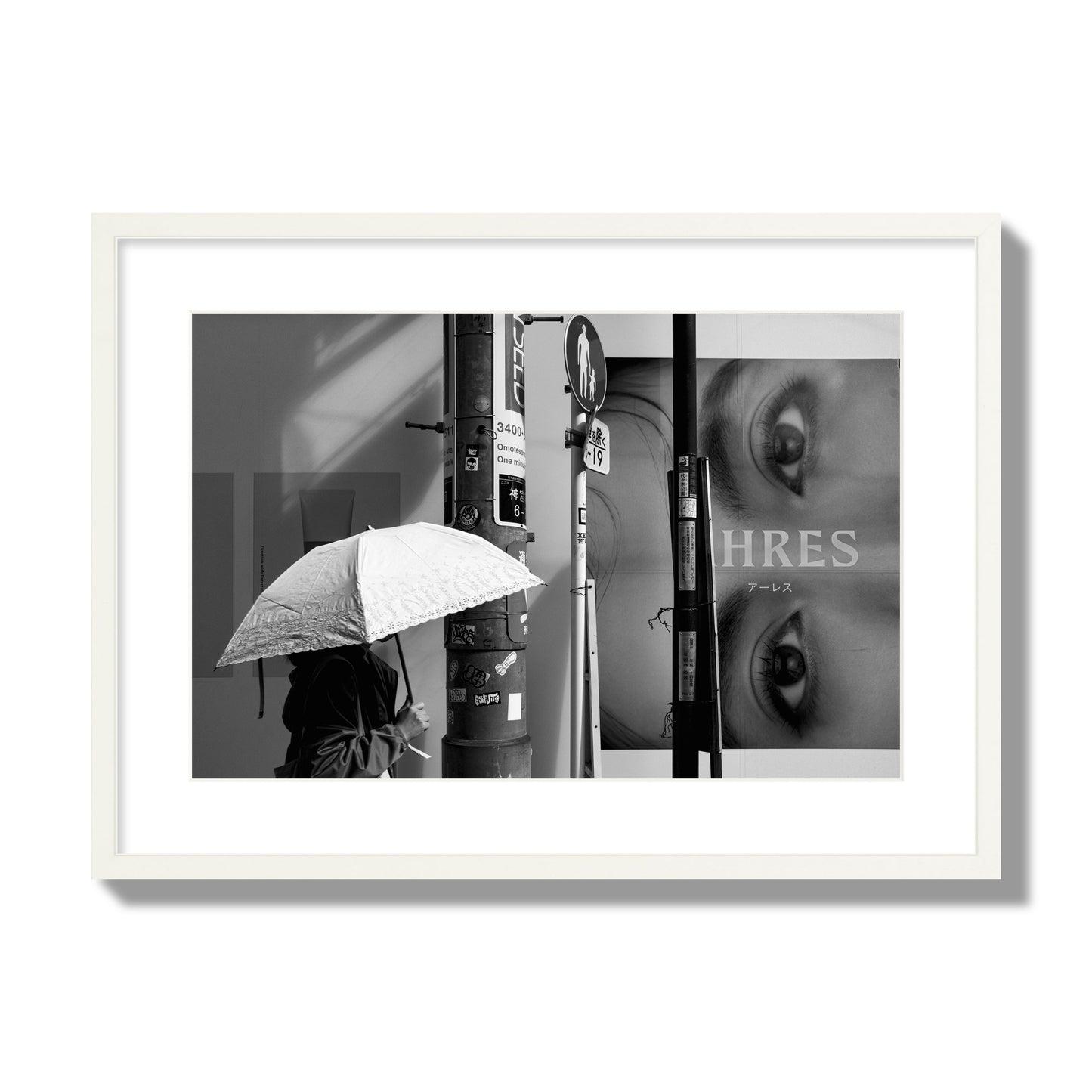 Fine art street photograph of a woman walking with an umbrella on a Tokyo street, passing beneath a billboard with two large eyes. Archival pigment print, large size, white frame.