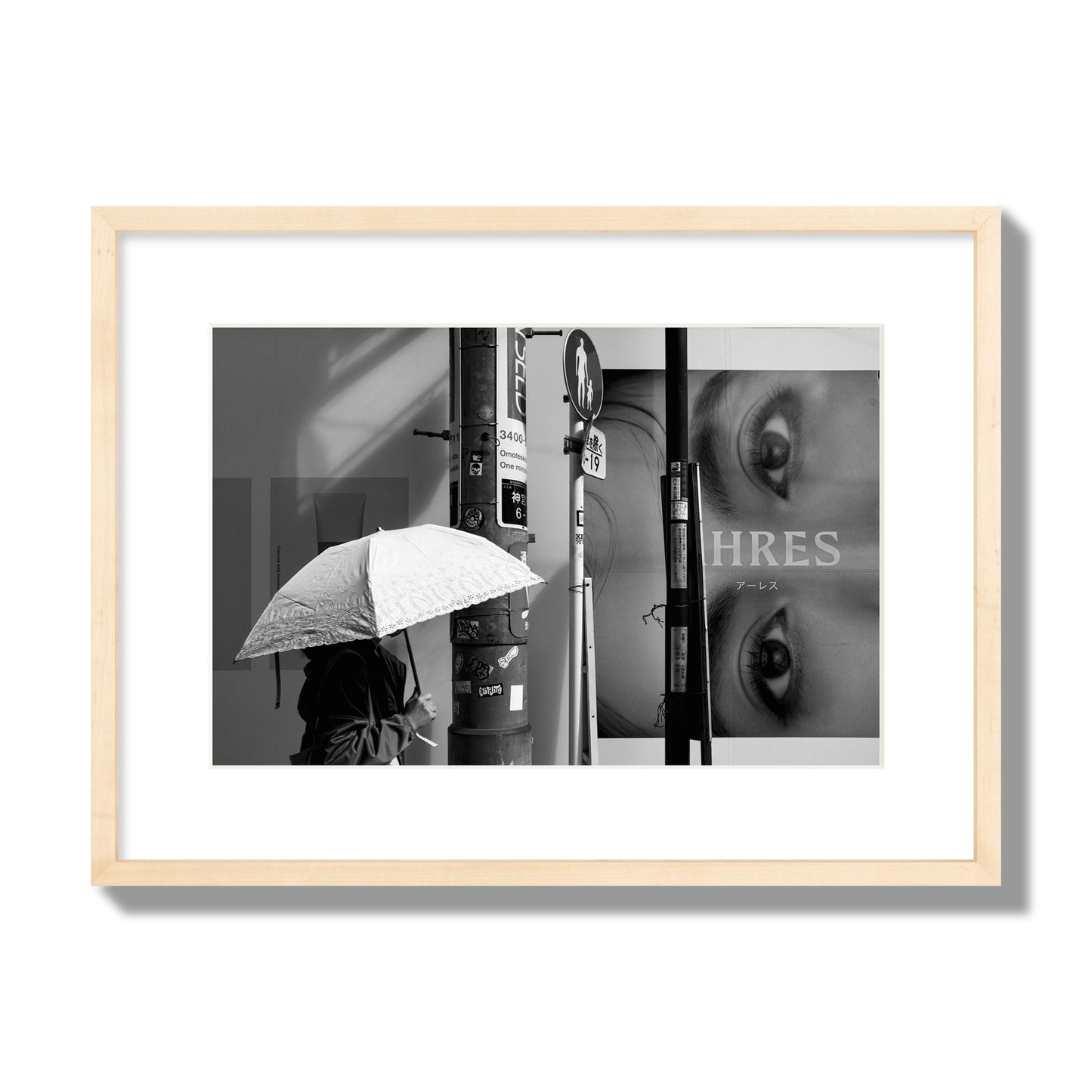 Fine art street photograph of a woman walking with an umbrella on a Tokyo street, passing beneath a billboard with two large eyes. Archival pigment print, medium size, natural wood frame.